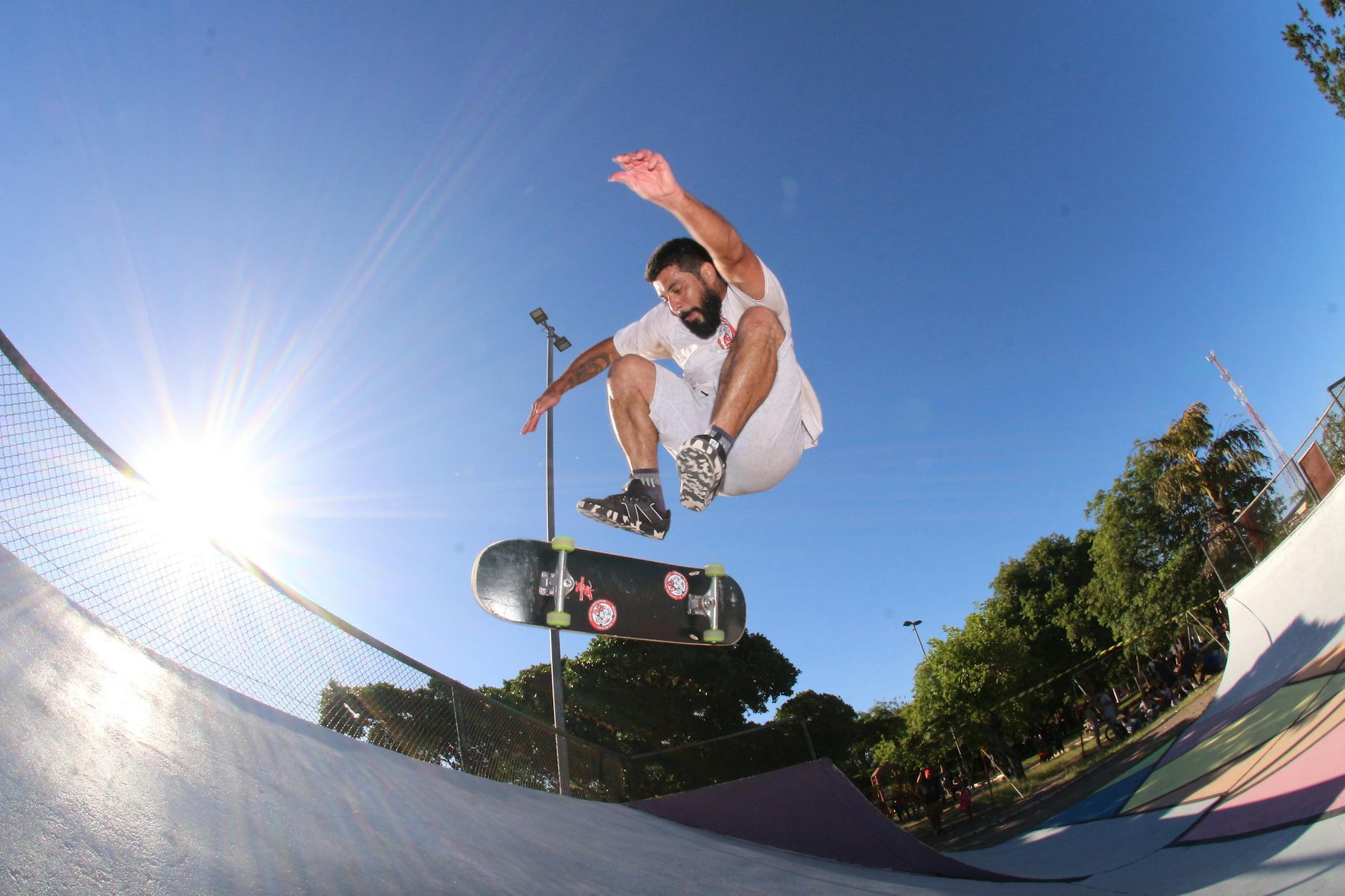 A skateboarder performs an aerial trick under a bright blue sky at a skatepark.