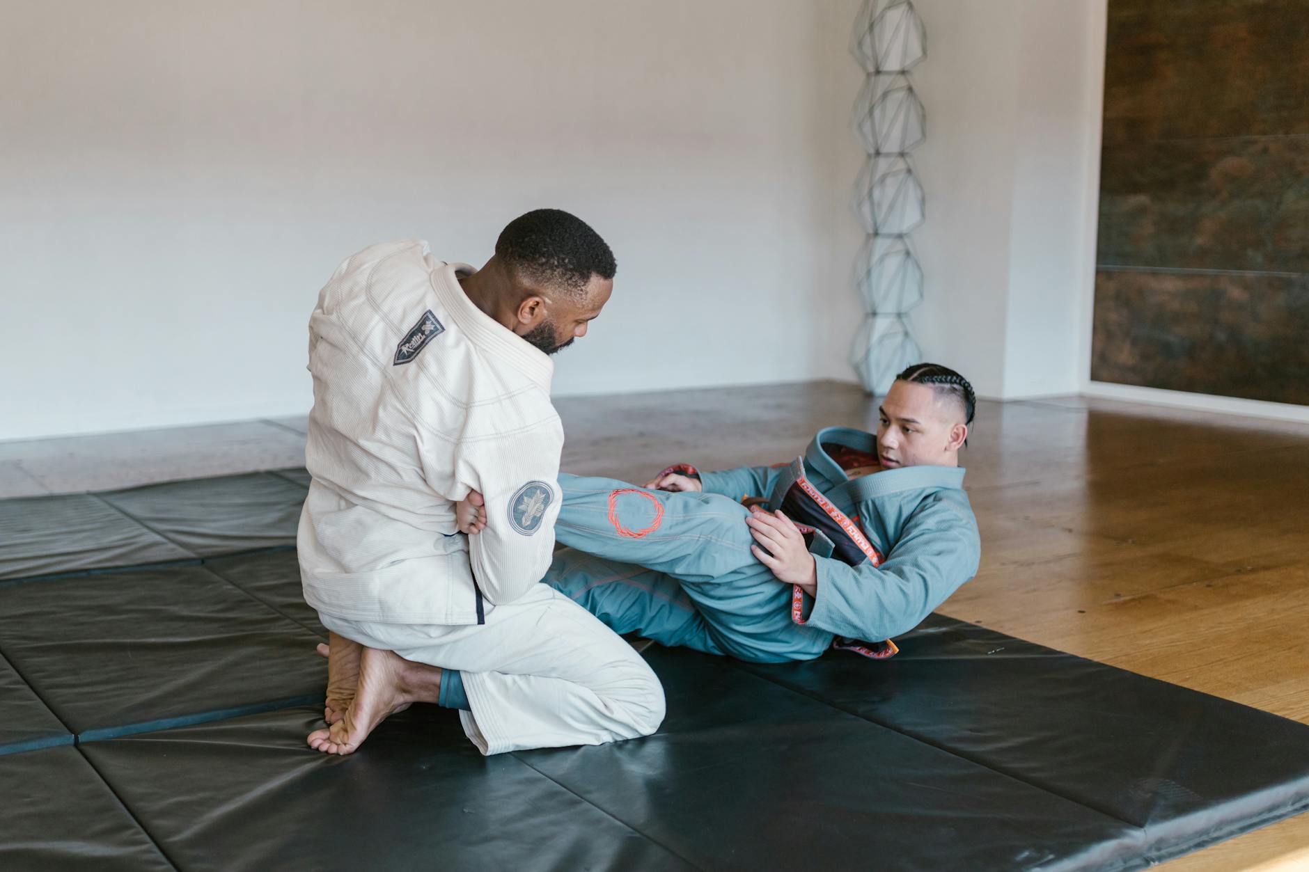 Two men engaged in Brazilian Jiu-Jitsu practice on a mat in an indoor training room.