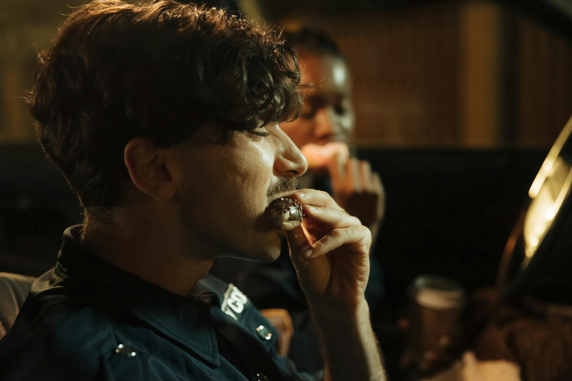 Two policemen enjoying doughnuts during a night shift in their patrol car.