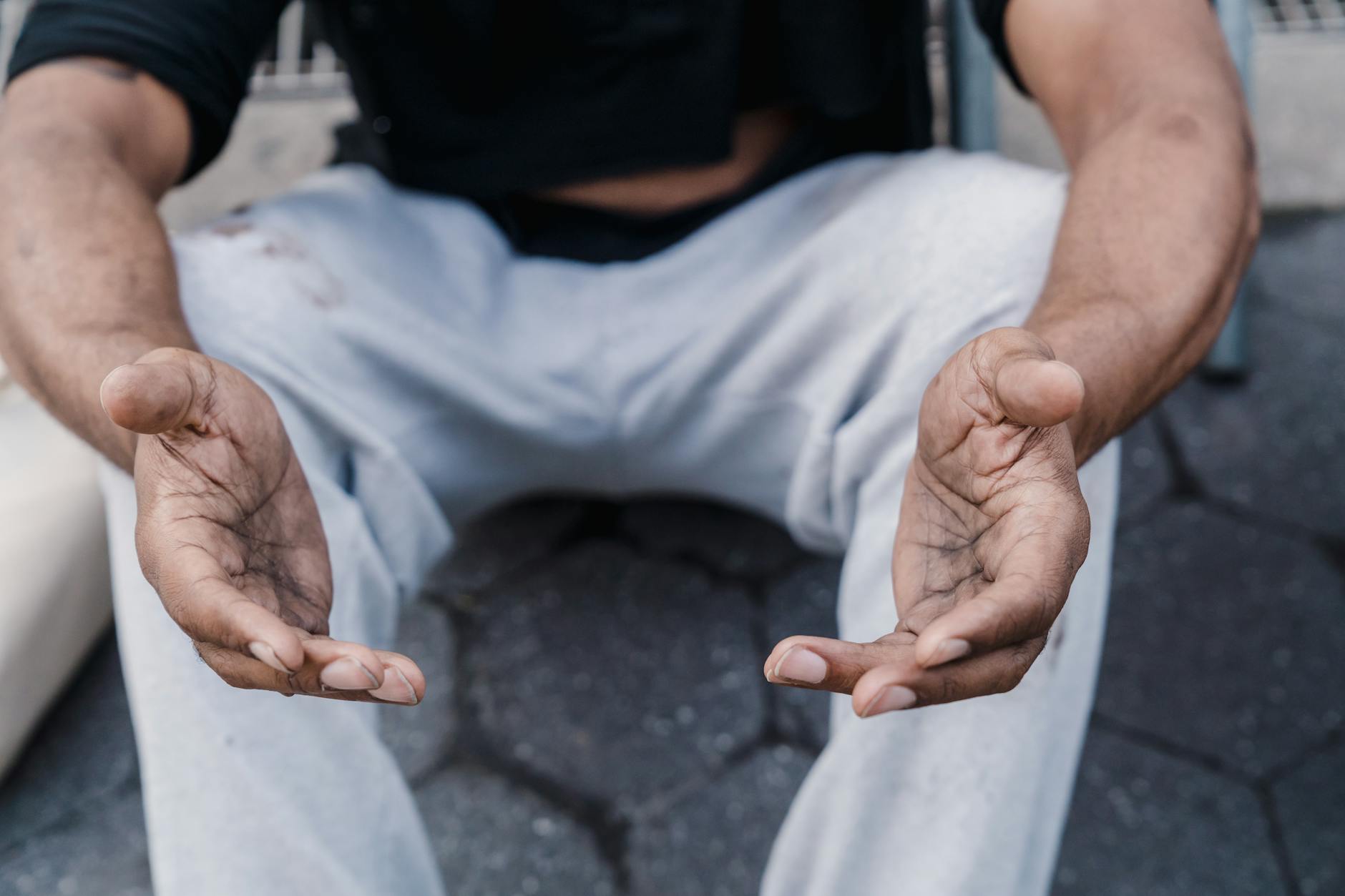 Close-up of outstretched hands of a seated person on a sidewalk, expressing openness.