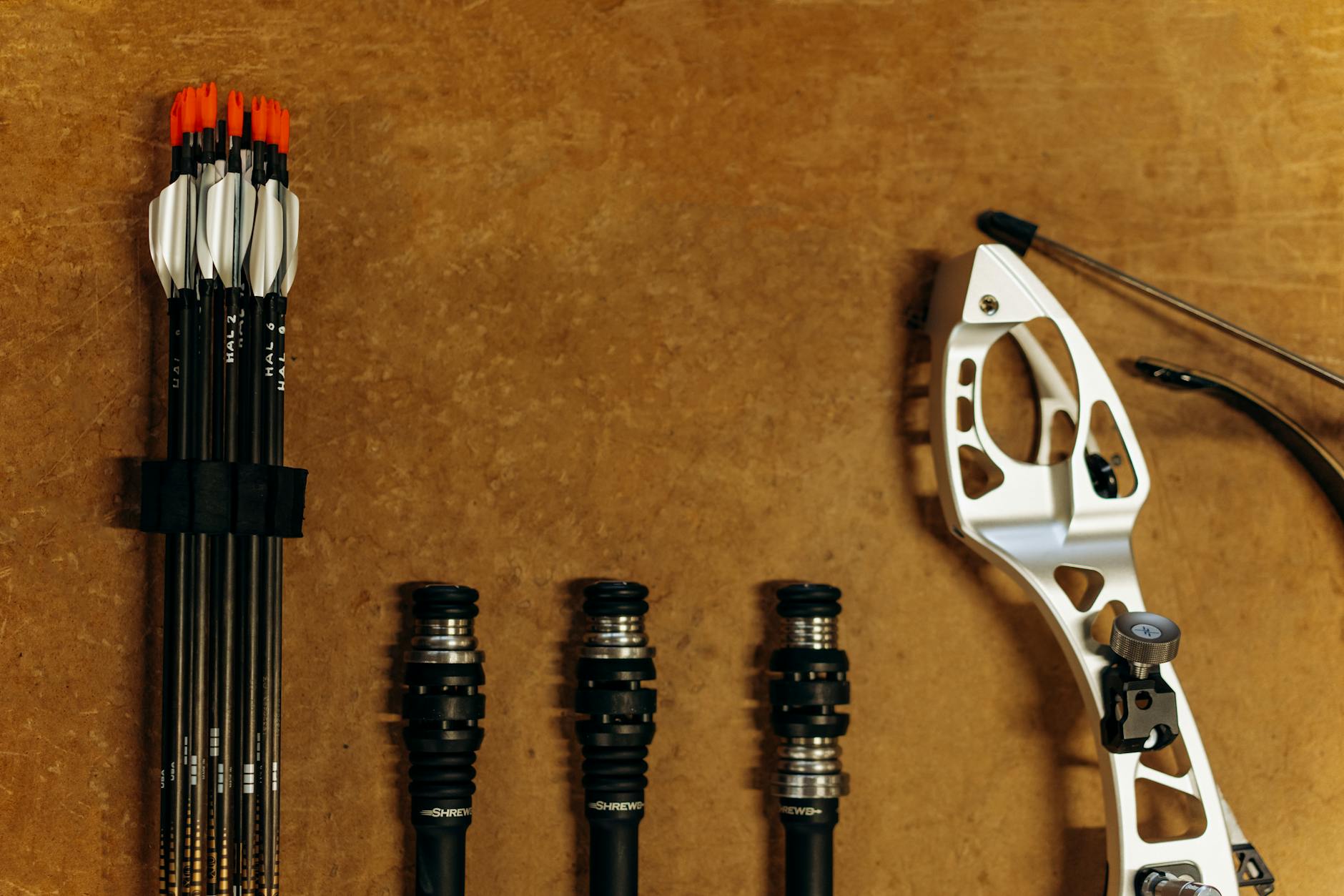 A detailed flat lay of archery equipment including arrows and a modern bow on a wooden surface.