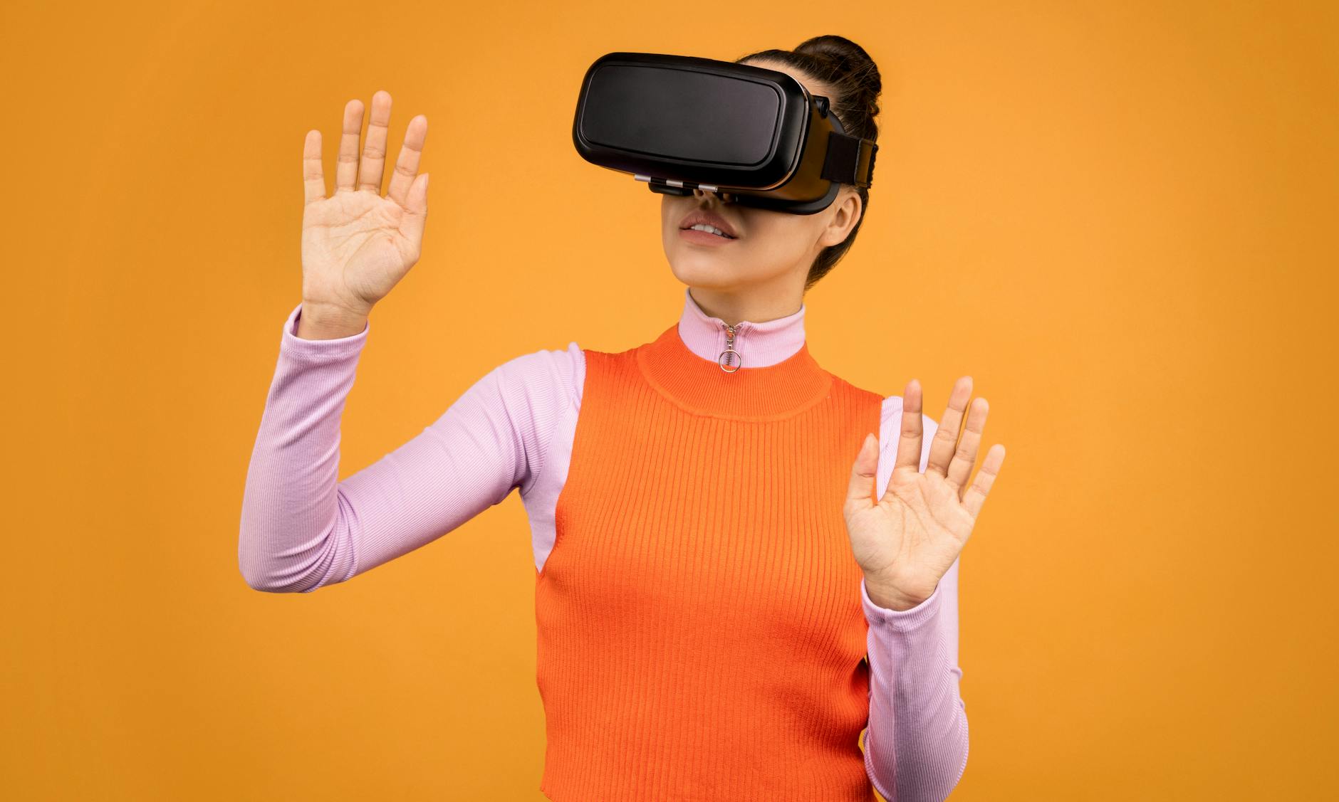 A young woman wearing VR goggles explores digital space against a yellow background indoors.