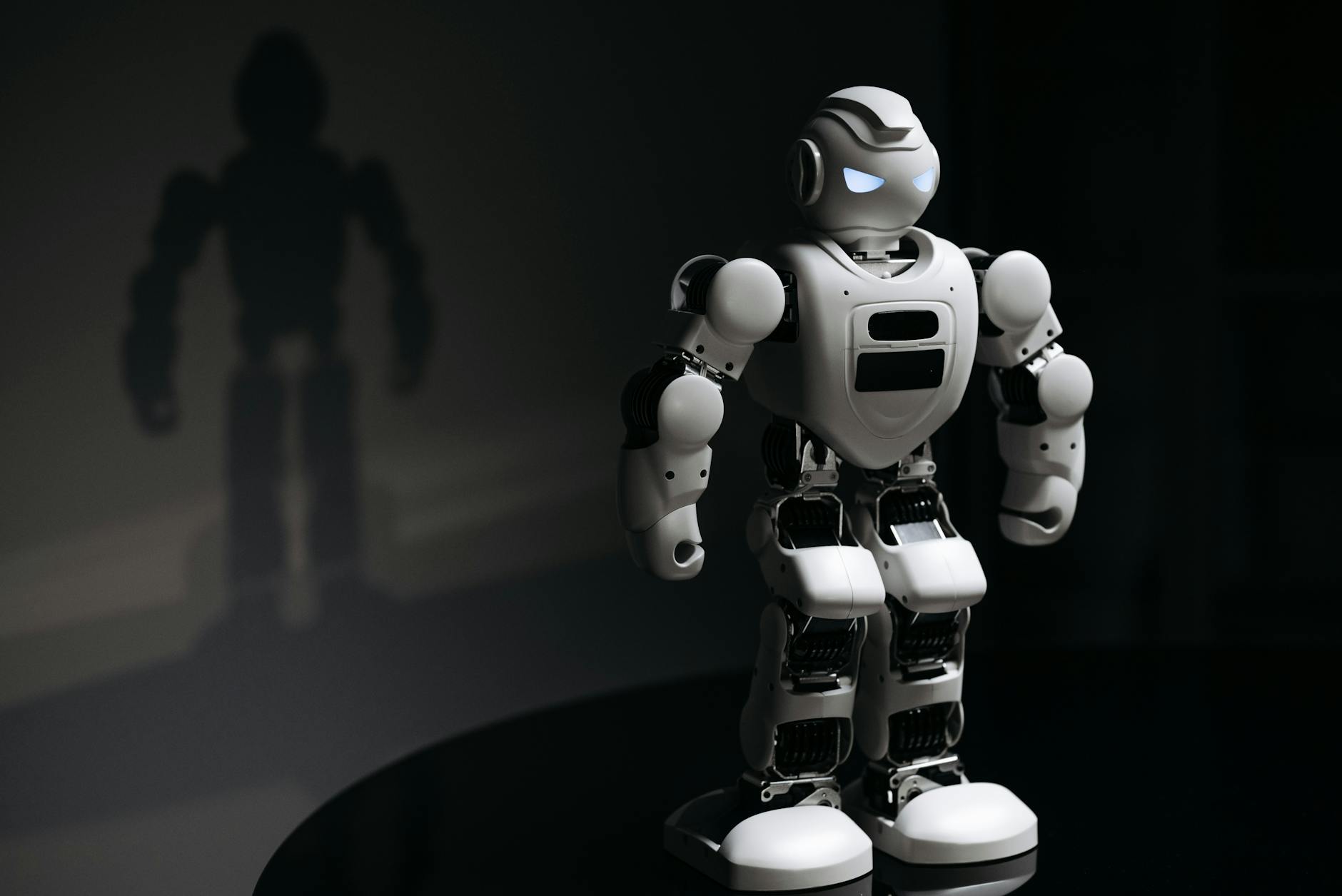 White robot toy casting a shadow in a dark studio setting, highlighting artificial intelligence.