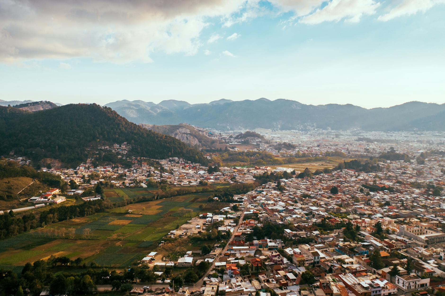 Scenic aerial view of a city with mountains in the background under a partly cloudy sky.