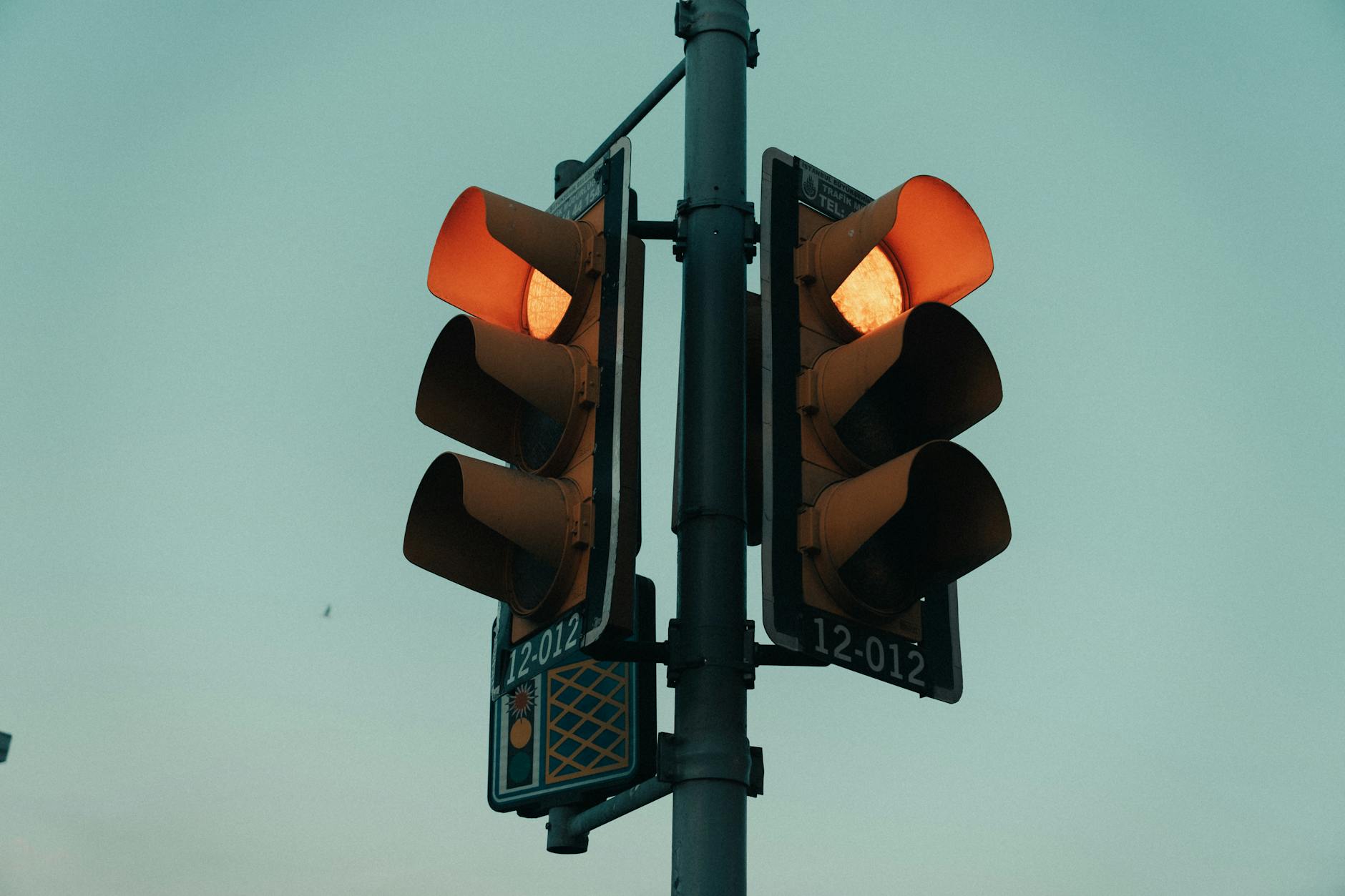 A close-up view of a traffic light glowing in an urban setting under the evening sky.