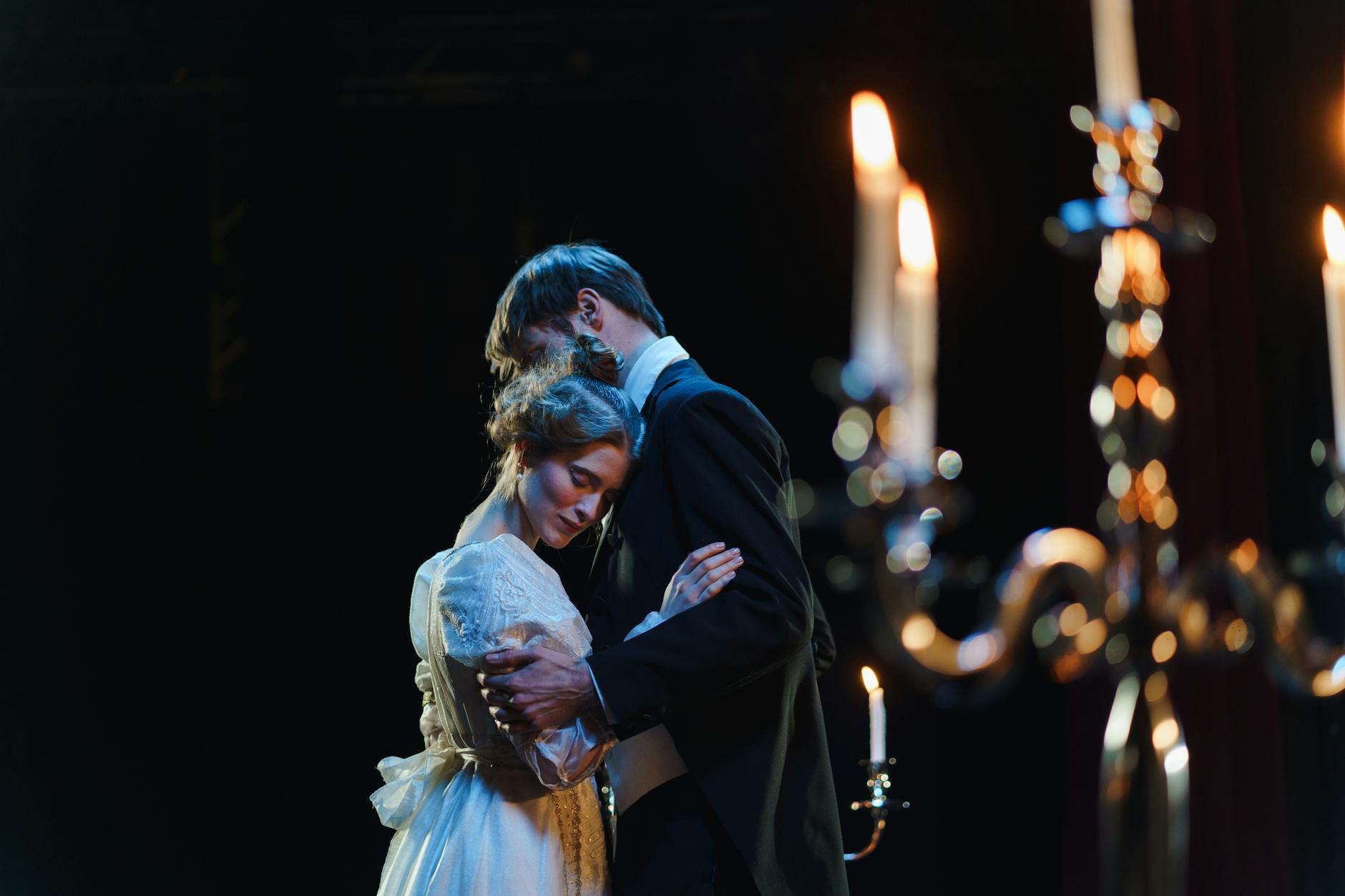A romantic embrace on stage between actors in elegant costumes under warm lighting.