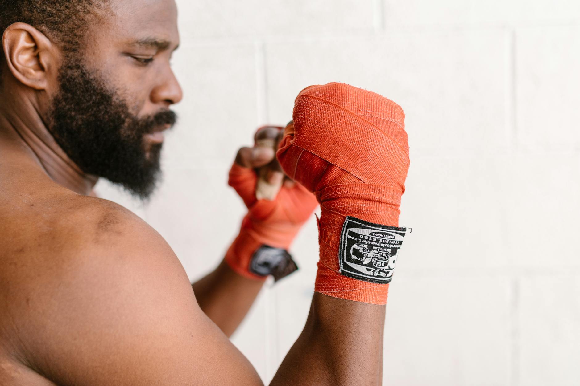 Profile of a boxer with beard and red hand wraps preparing for training session.
