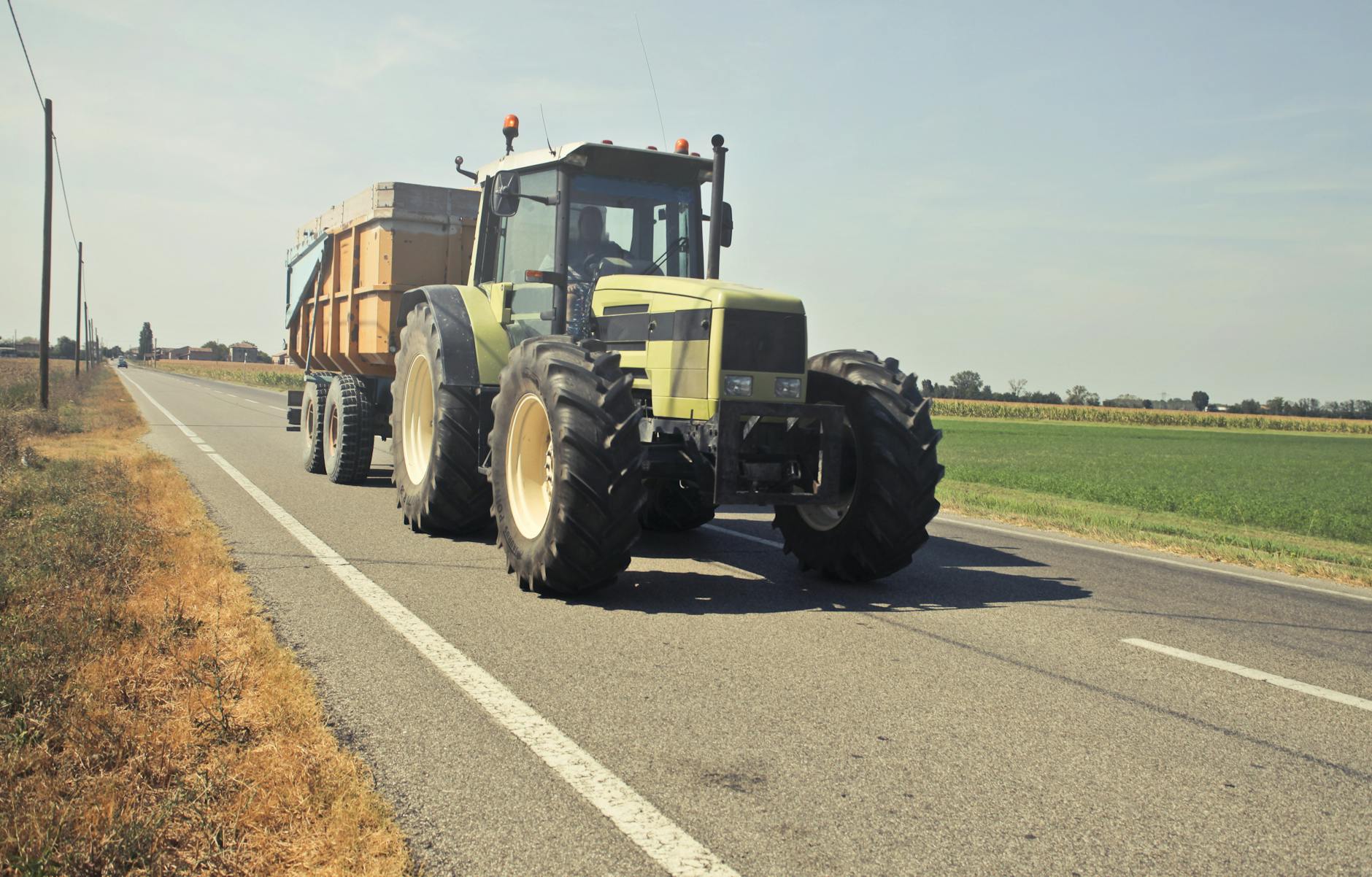 A tractor with a trailer driving on a rural road in the Italian countryside.