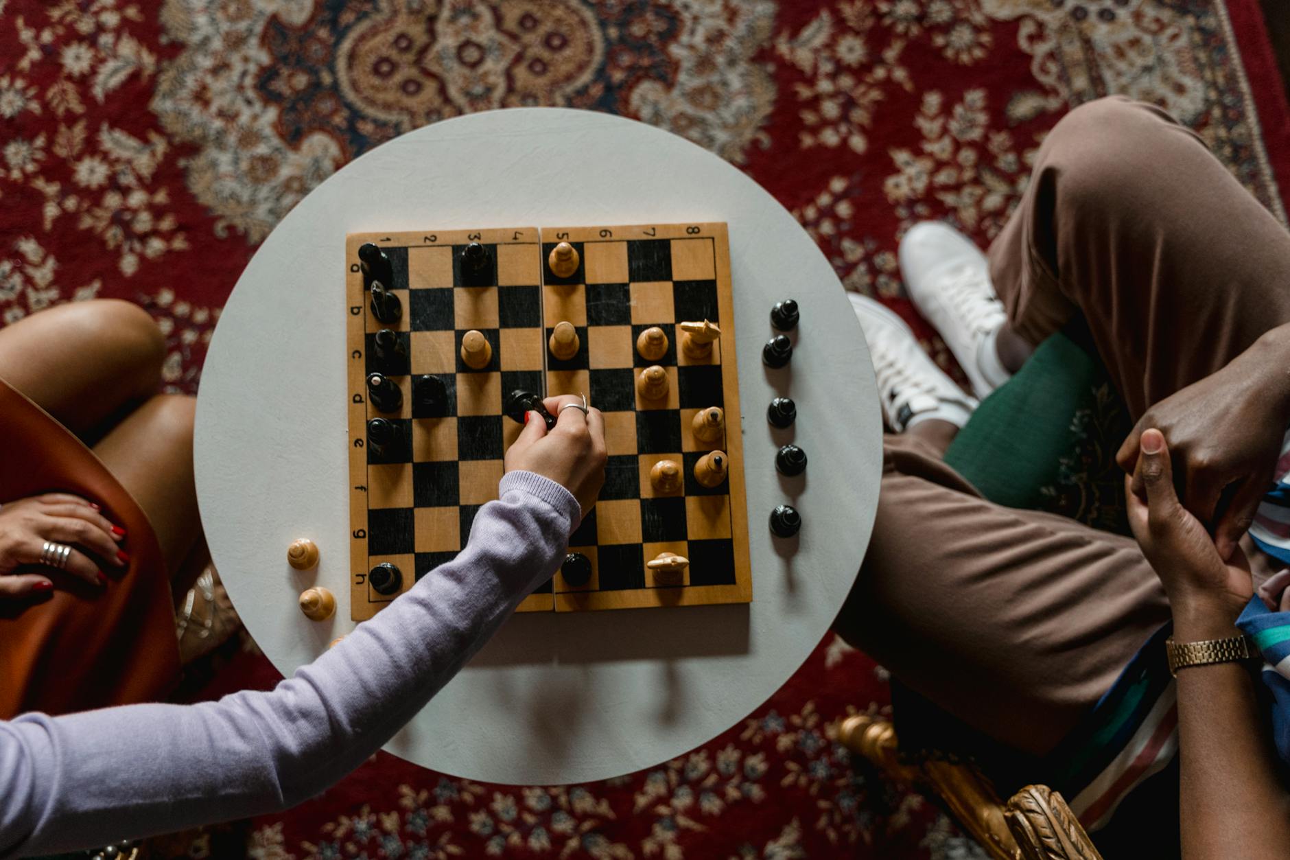 A top view of two people playing chess on a round table indoors, highlighting strategic gameplay.