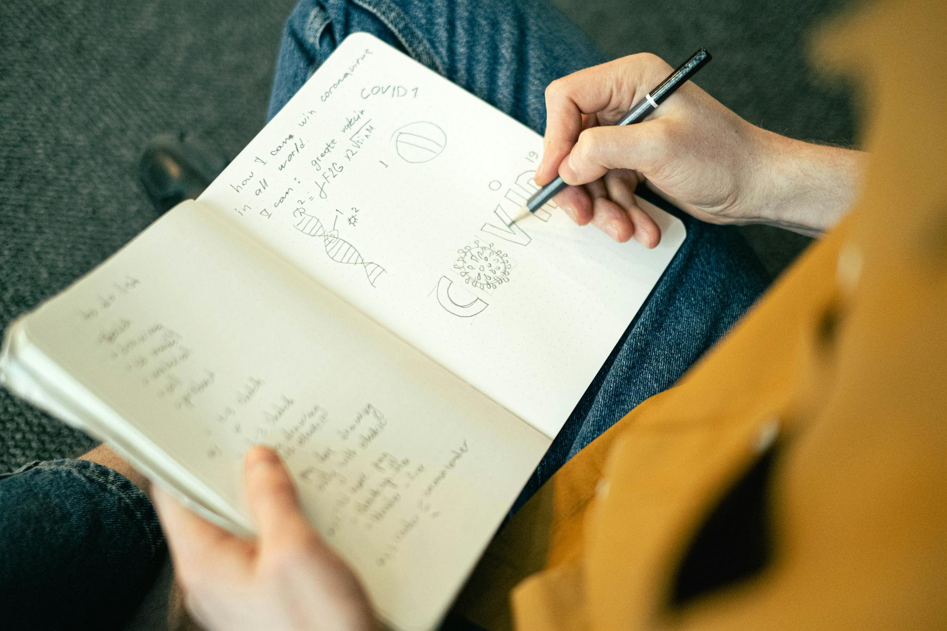 Close-up of a person writing COVID-19 related notes in a sketchbook, featuring sketches and writing.