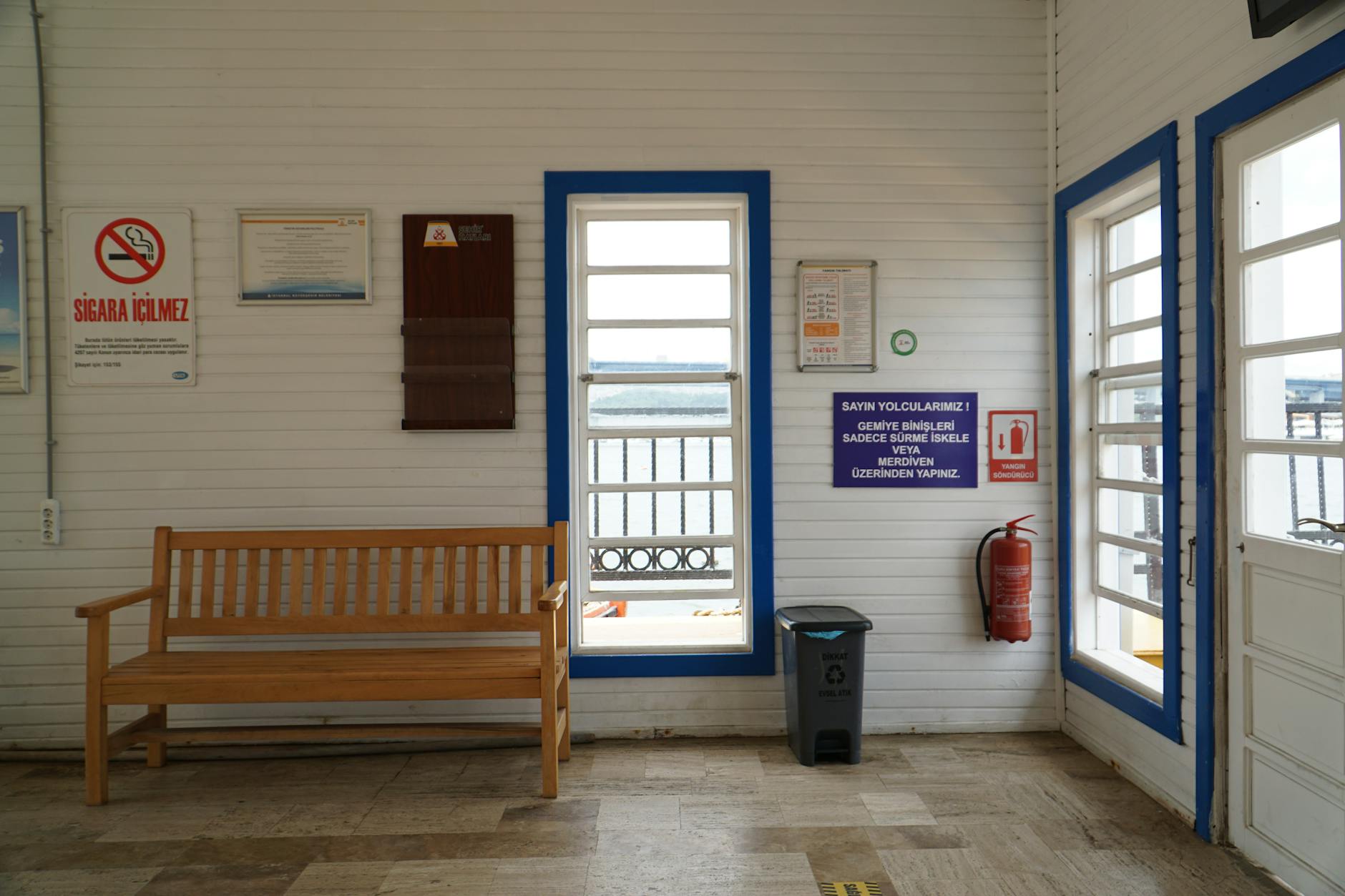 Cozy indoor waiting area in Istanbul with a wooden bench and various signs on white paneled walls.