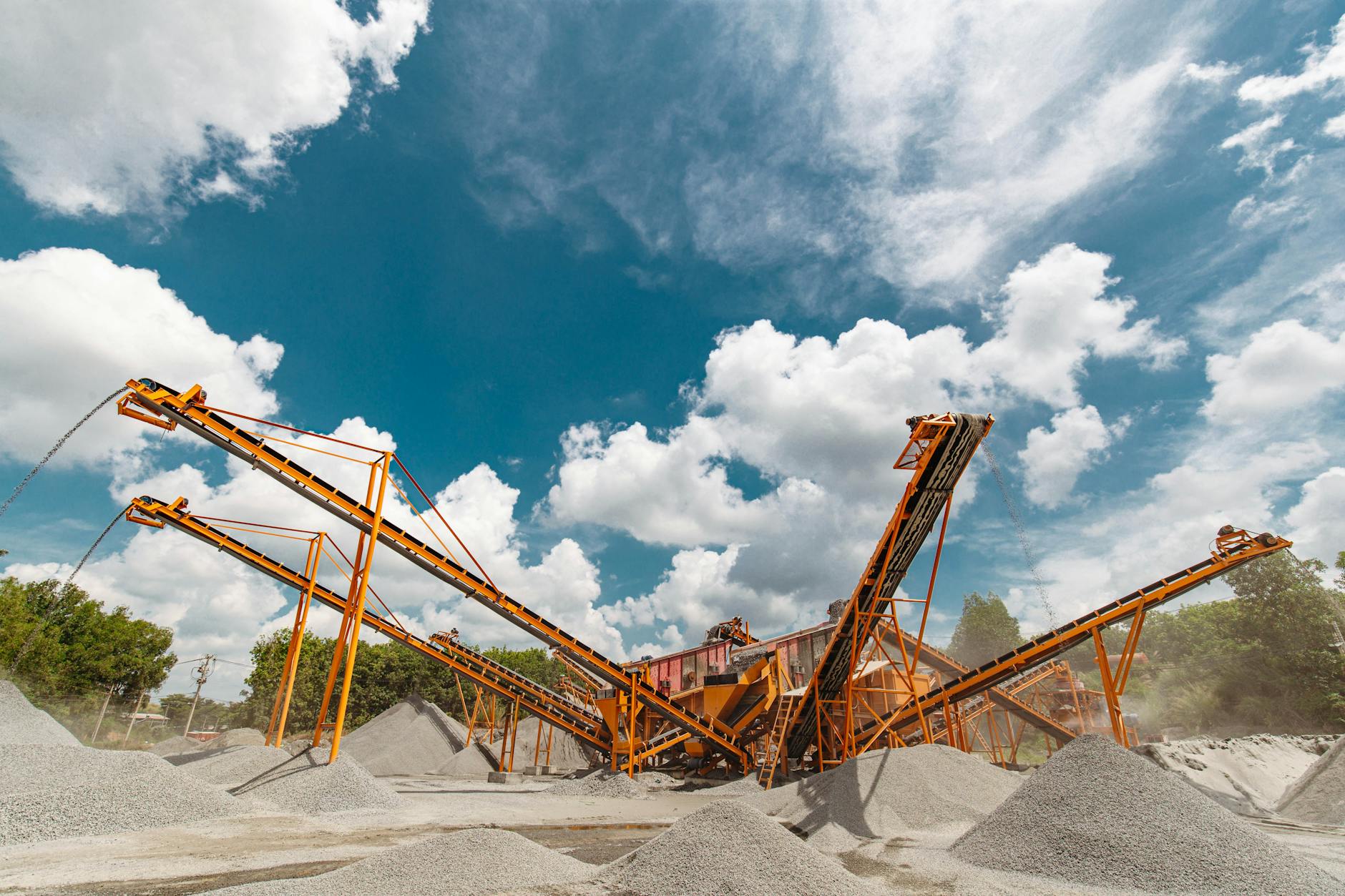 Vibrant conveyor belts moving gravel under a clear blue sky in an industrial quarry setting.