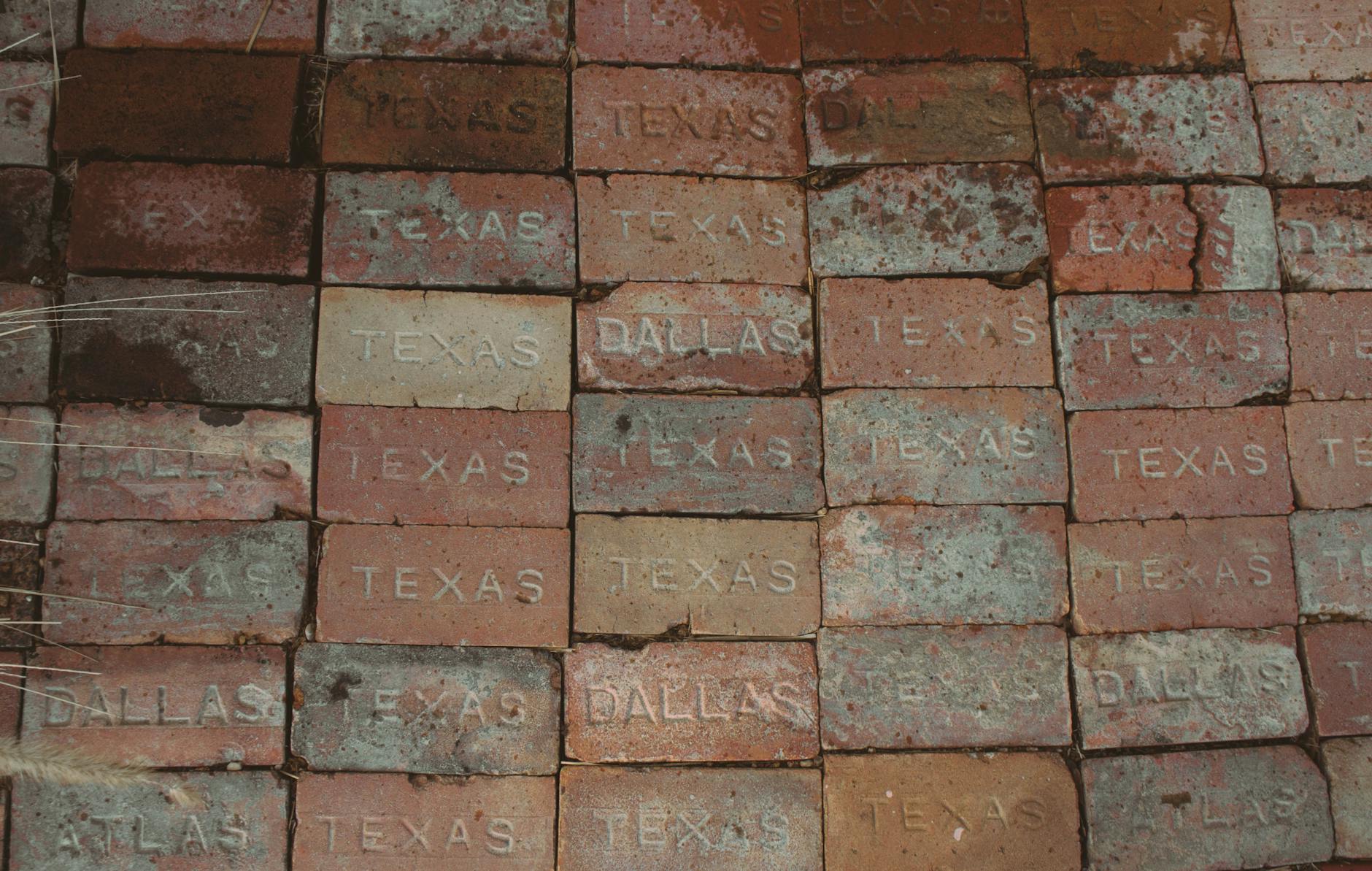 Close-up of stacked bricks engraved with 'Texas' and 'Dallas'. Rustic, textured surface.