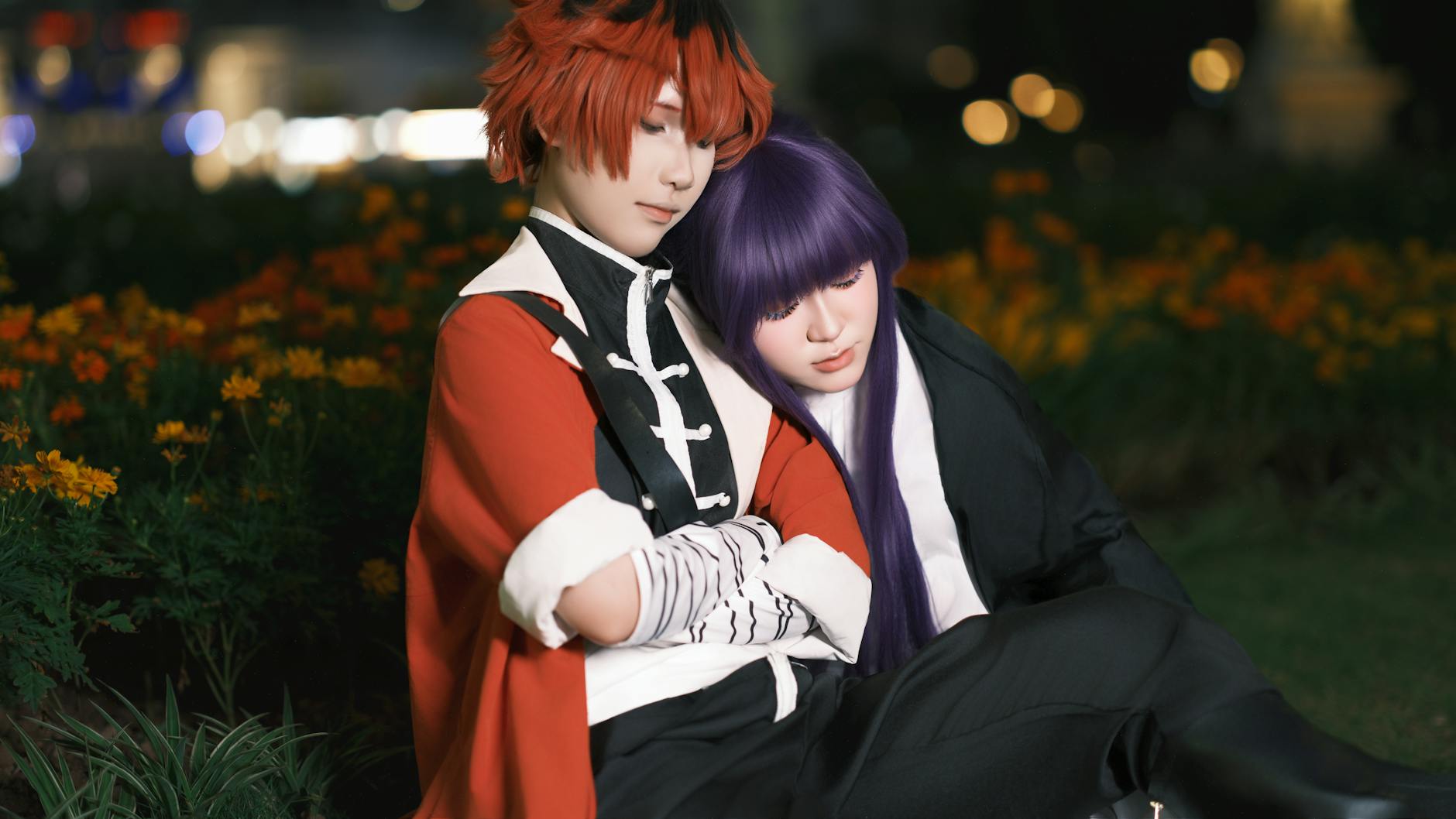 Two cosplayers in detailed costumes sit closely in a garden at night.