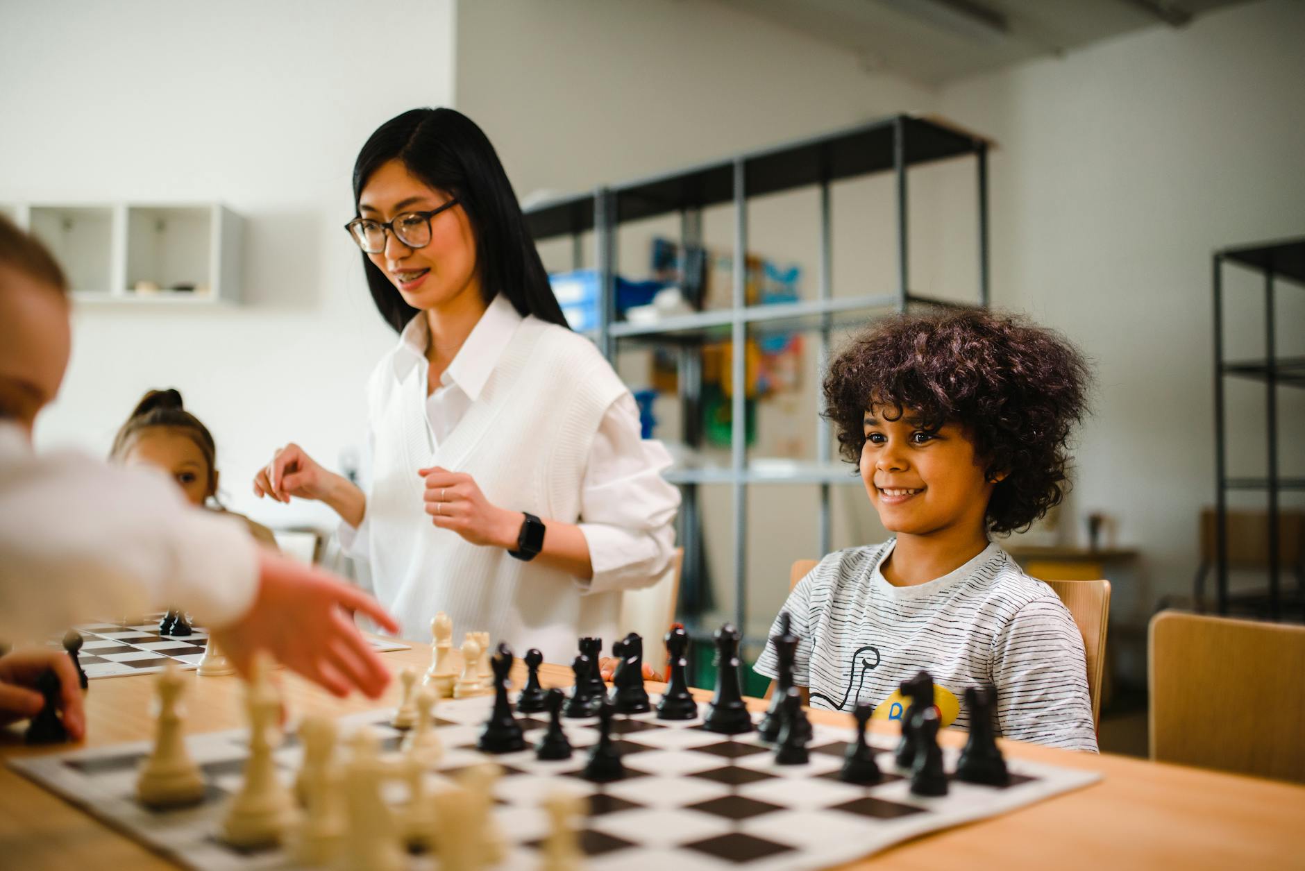 Children playing chess in a classroom setting guided by a teacher, emphasizing learning and fun.