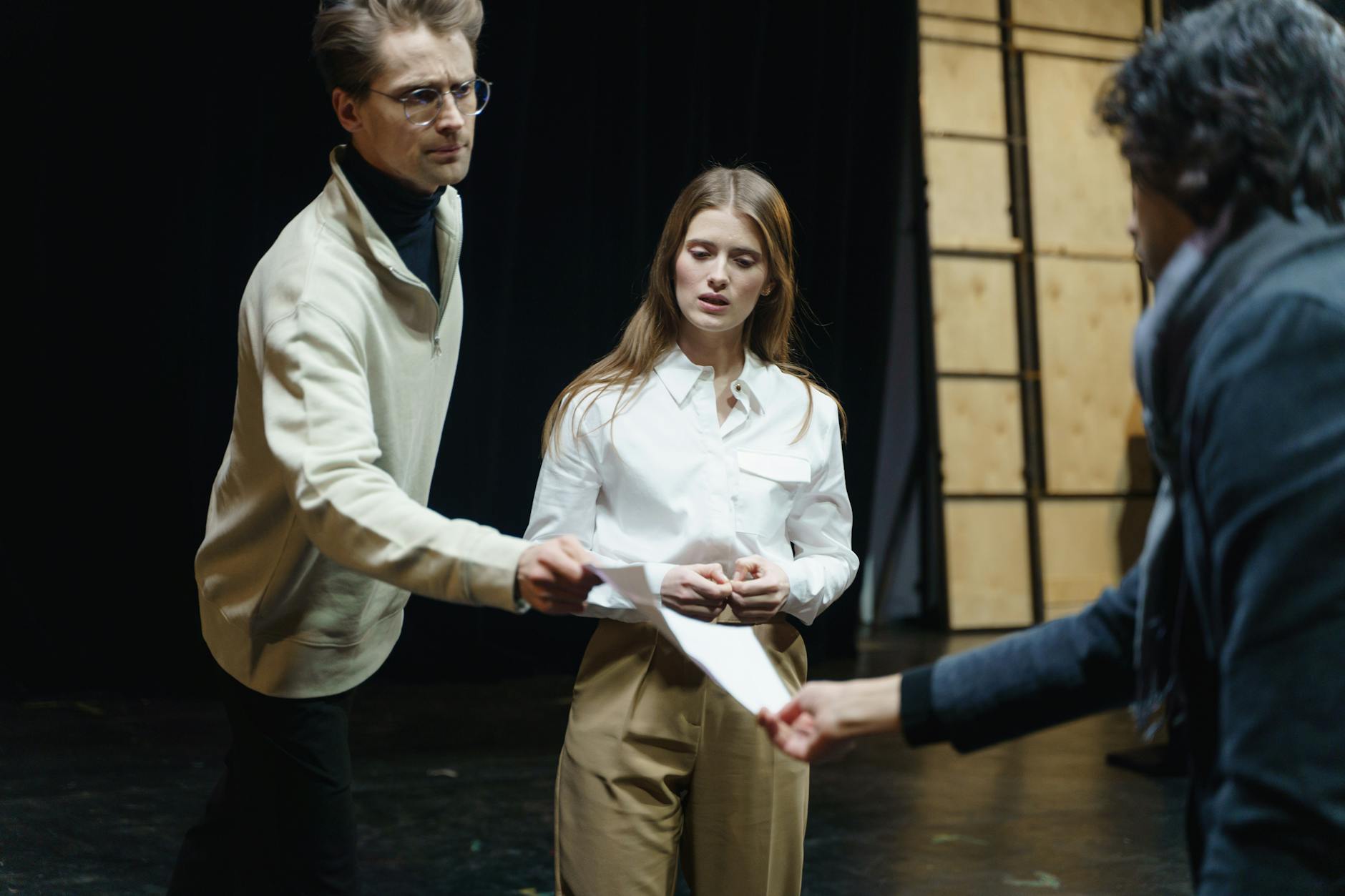 Actors engage in a rehearsal, exchanging scripts on stage, embodying theatrical drama and emotion.