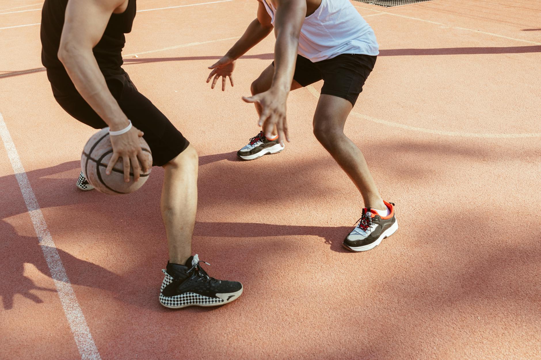 Two men engage in a lively basketball match on an outdoor clay court during the day.