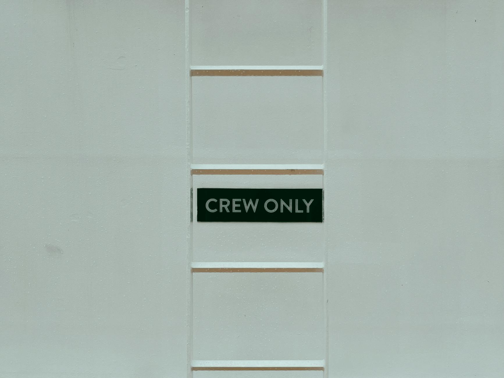 A minimalistic image featuring a 'Crew Only' sign on a ladder against a white wall.