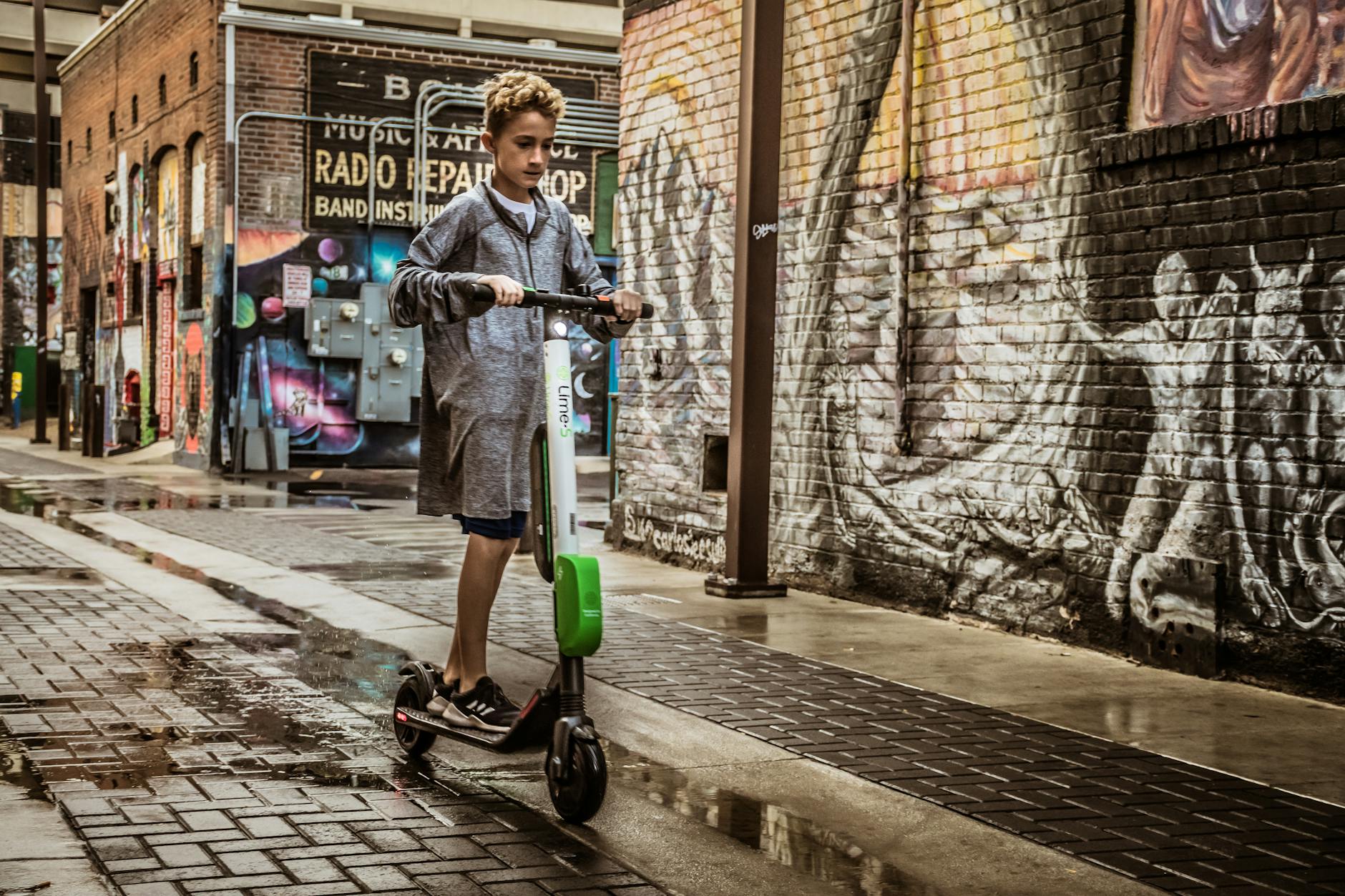 Child riding an electric scooter through a graffiti-covered urban alleyway.