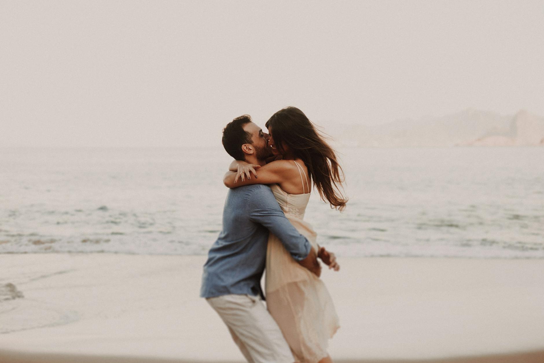 A couple shares a romantic embrace by the ocean, capturing a moment of love.