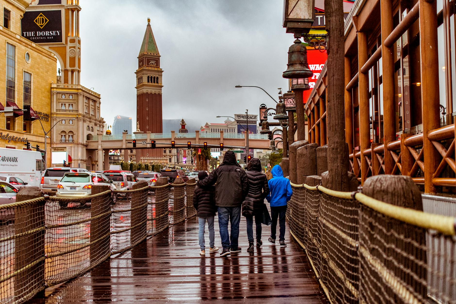 People walking along a wet street in Las Vegas with iconic architecture and a cloudy sky.