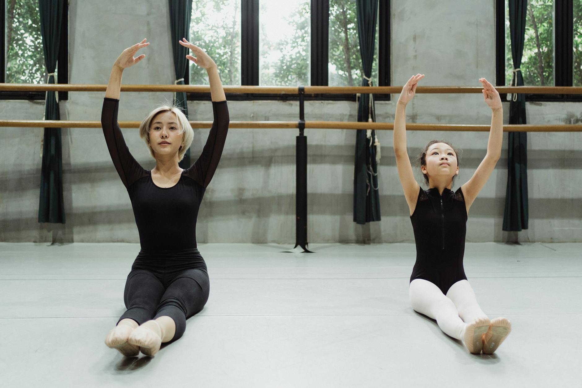 An Asian woman and child practice ballet in a studio, arms raised in perfect form.