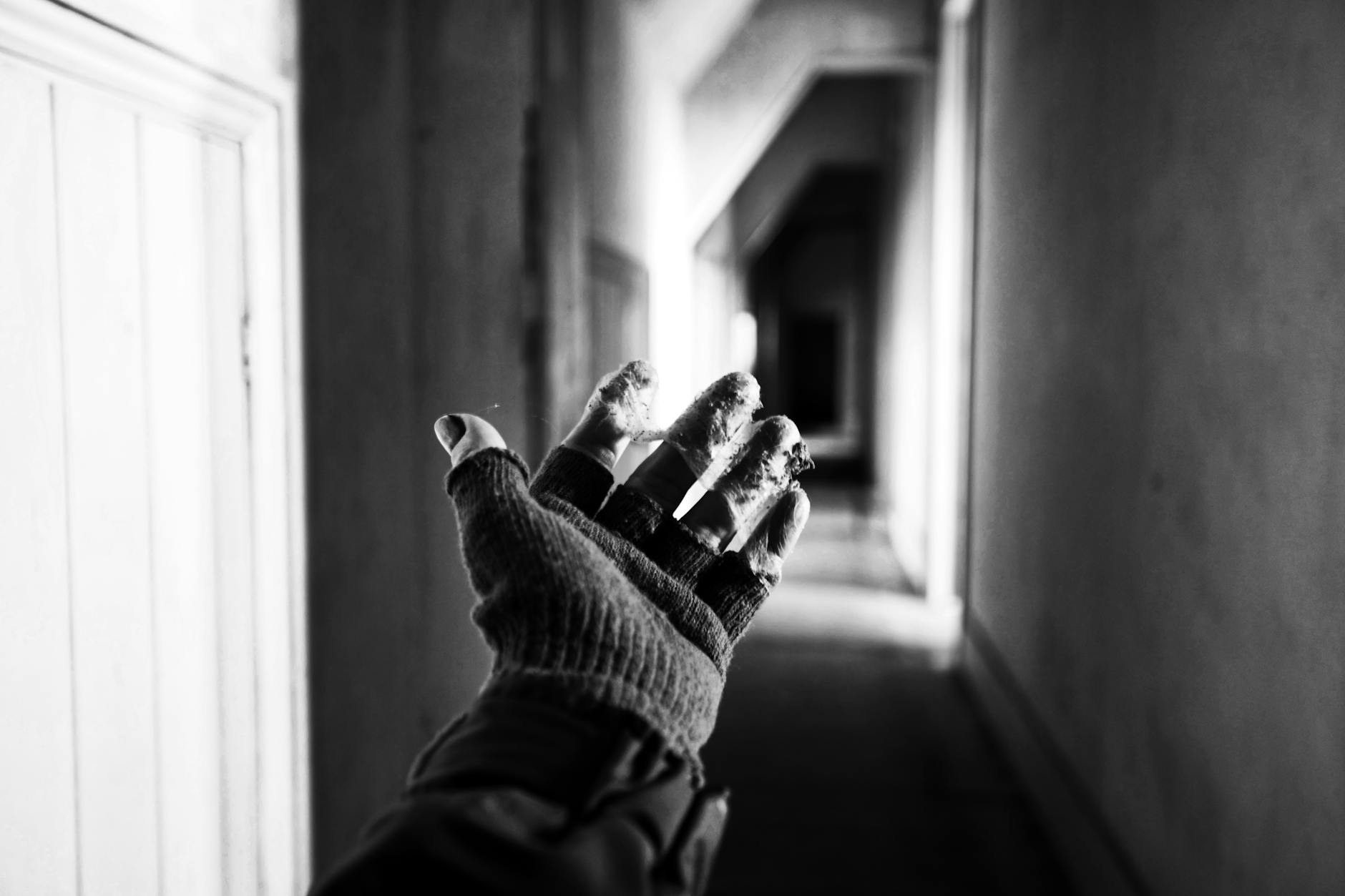 Black and white image of a gloved hand reaching in a dimly lit corridor.