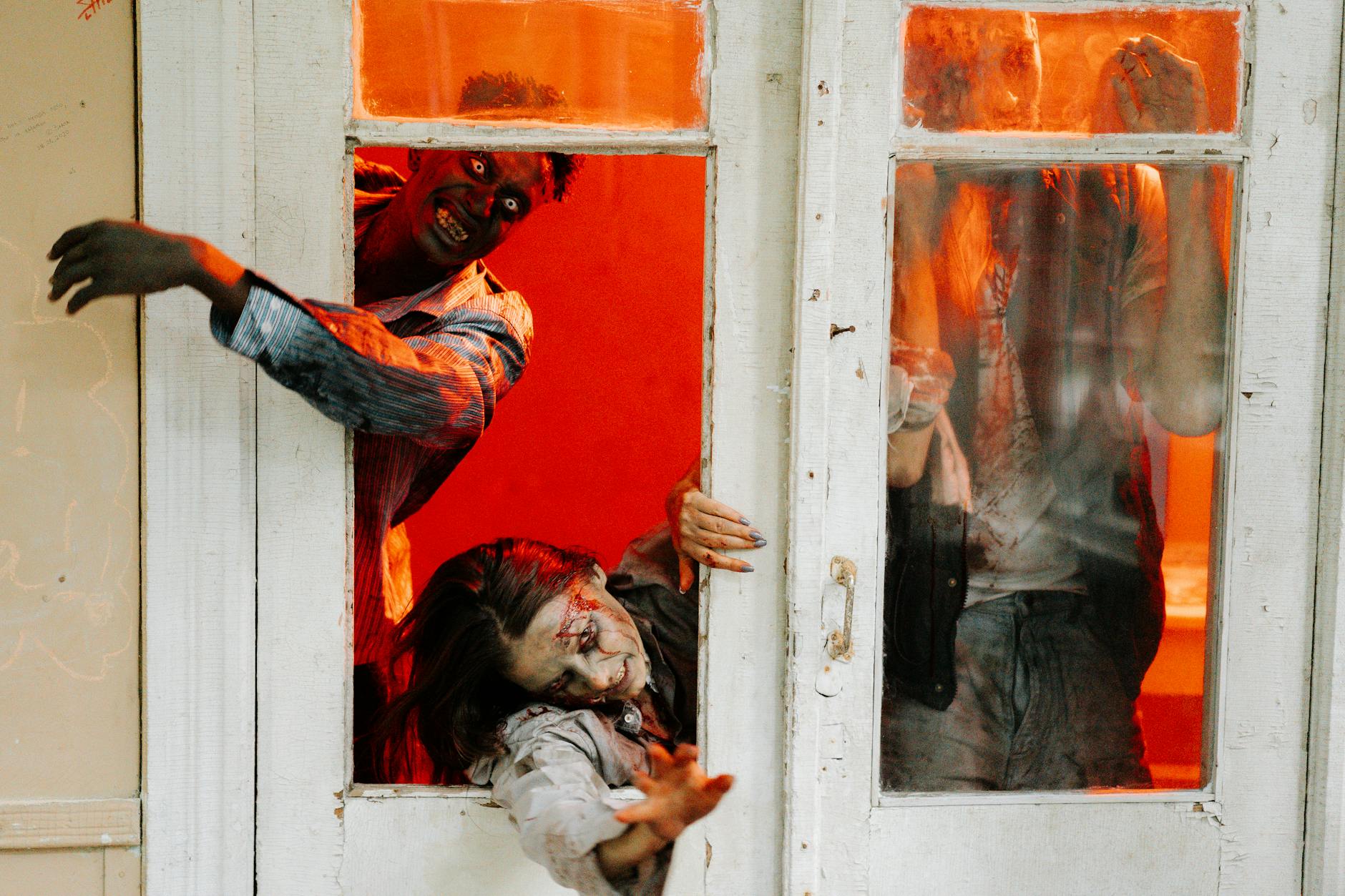 Zombies breaking through a door in a vivid horror scene with intense red lighting.