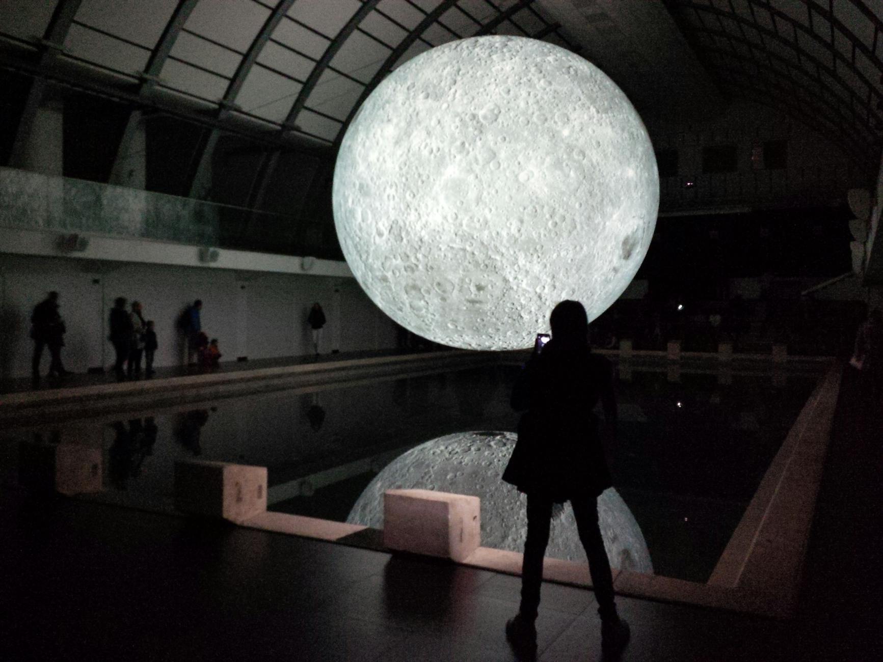 Captivating indoor display of a large moon replica with its reflection in a pool.