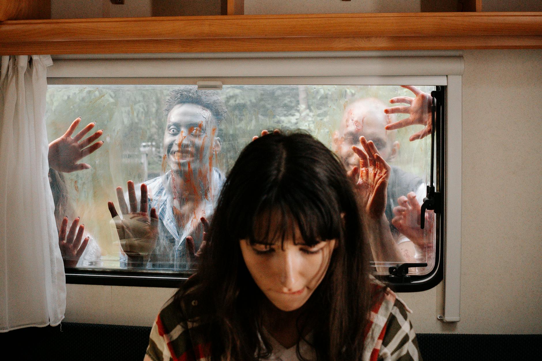 A woman sits unaware while terrifying zombies threaten through the window.