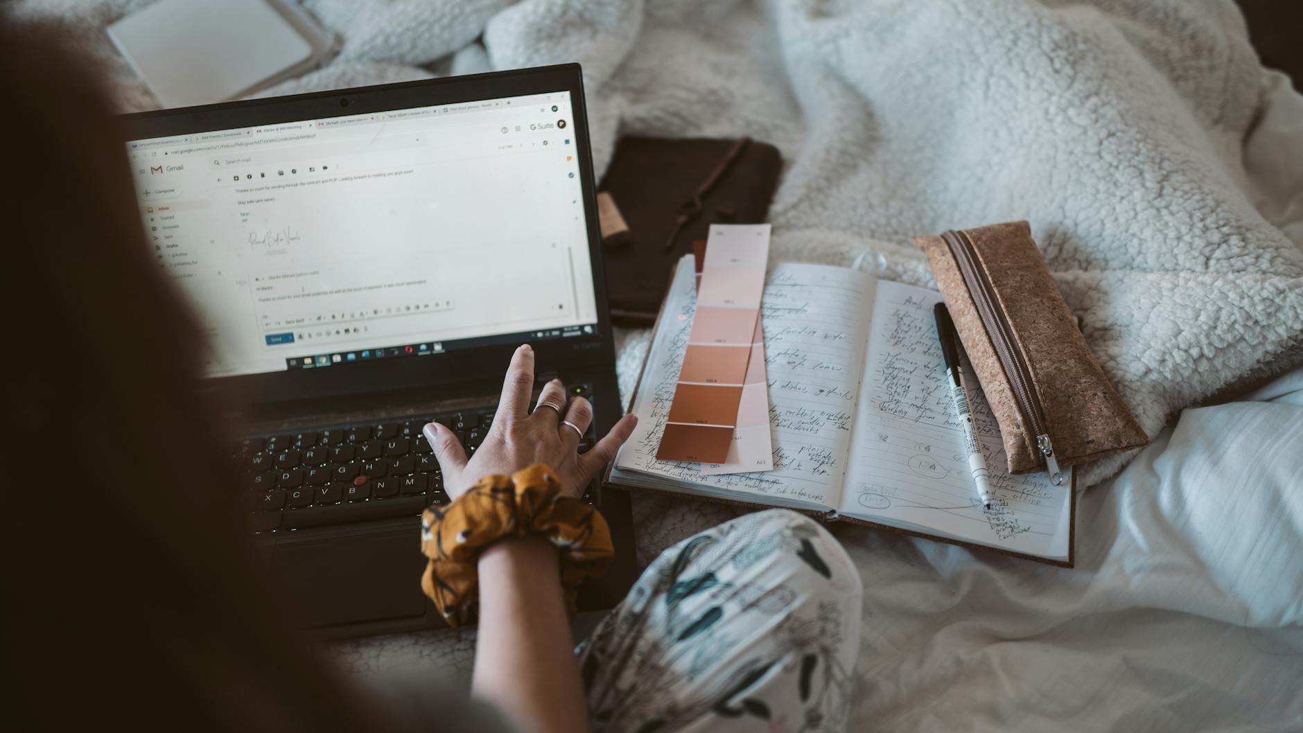 Woman working from home using a laptop, surrounded by notes and stationery.