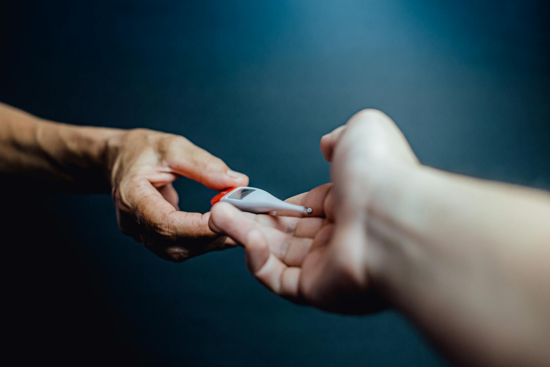 Close-up of two hands passing a thermometer, symbolizing healthcare collaboration.