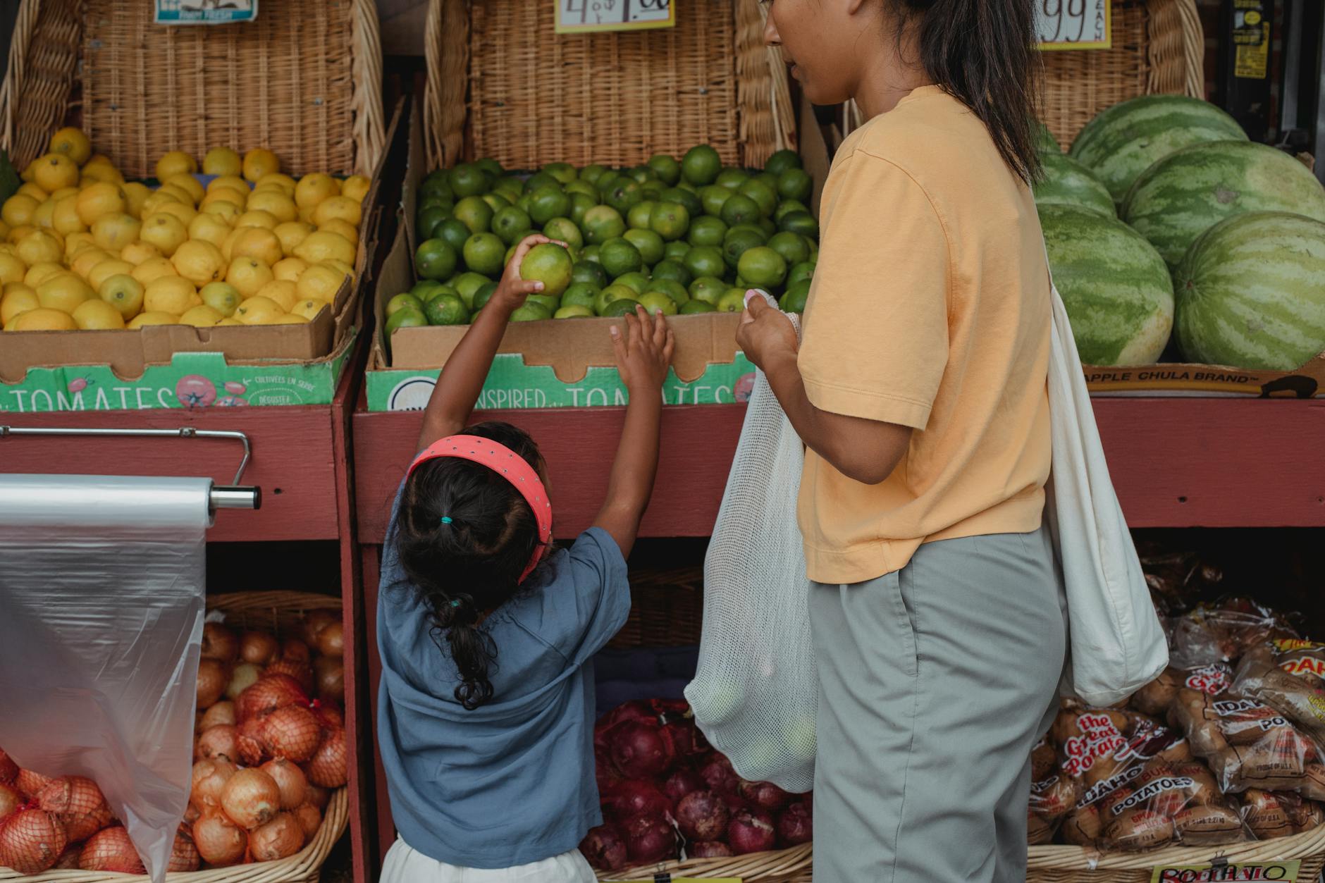 A mother and her daughter select fresh fruits from a market, emphasizing healthy and eco-friendly choices.