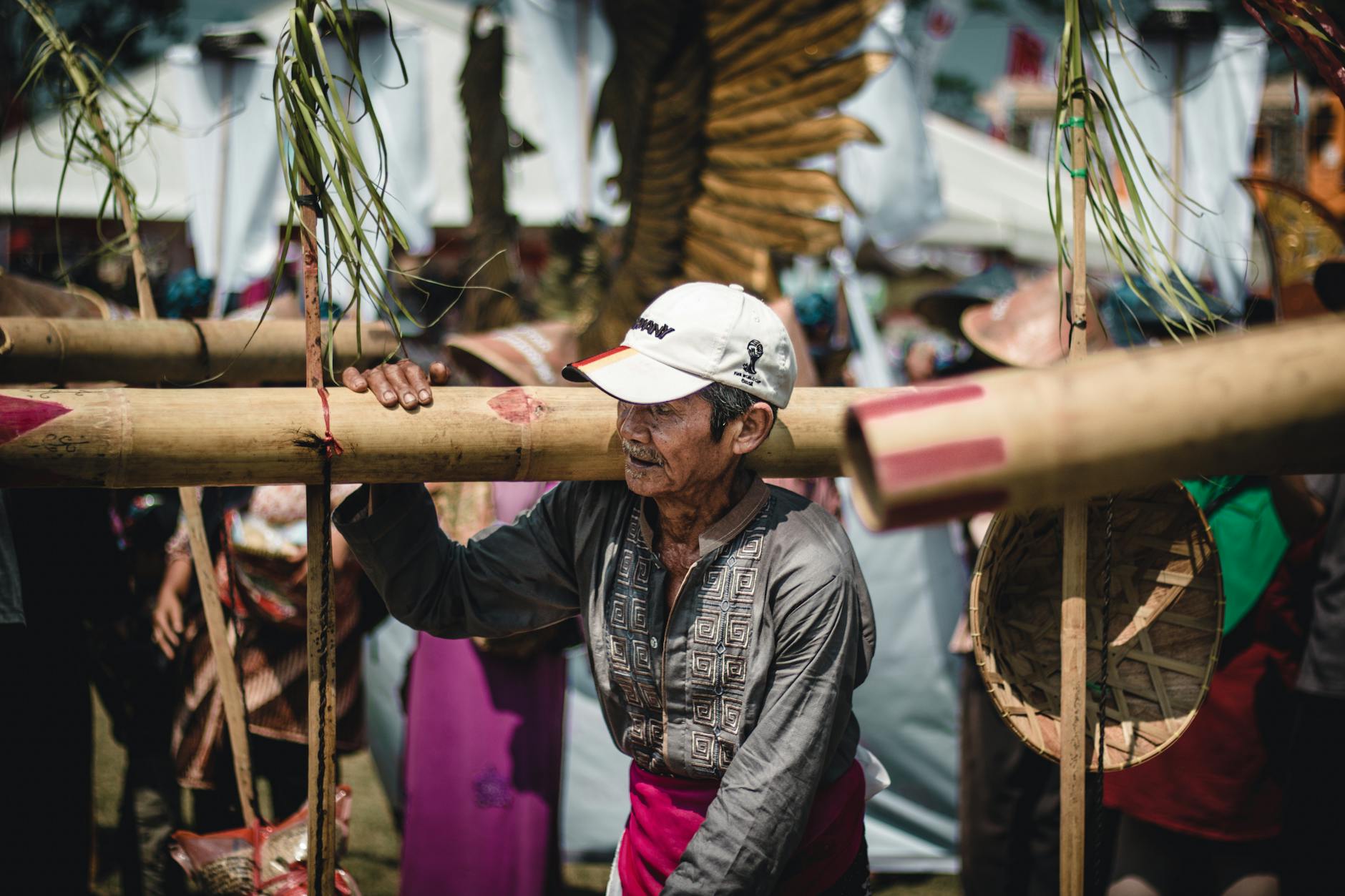 Serious mature Asian male in casual clothes walking with long bamboo stem on shoulder in local village