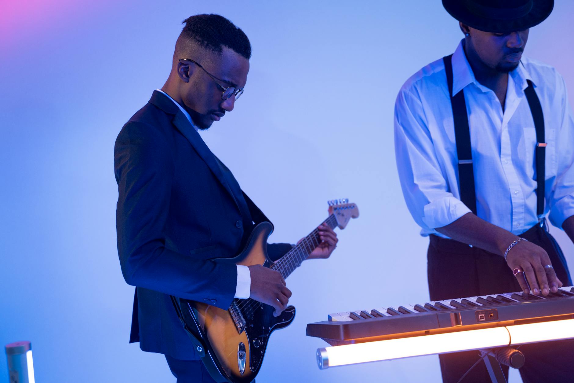 Two male musicians performing with an electric guitar and keyboard in a modern studio setting.