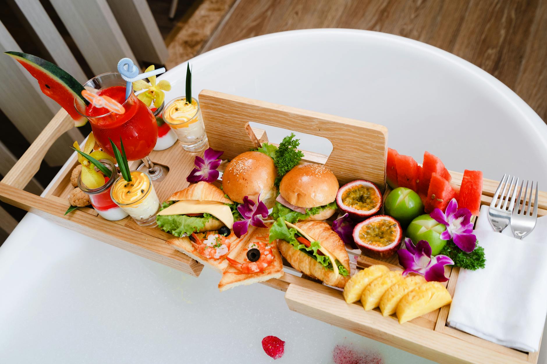 Deluxe breakfast platter served on a bathtub tray with fruits, sandwiches, and drinks.