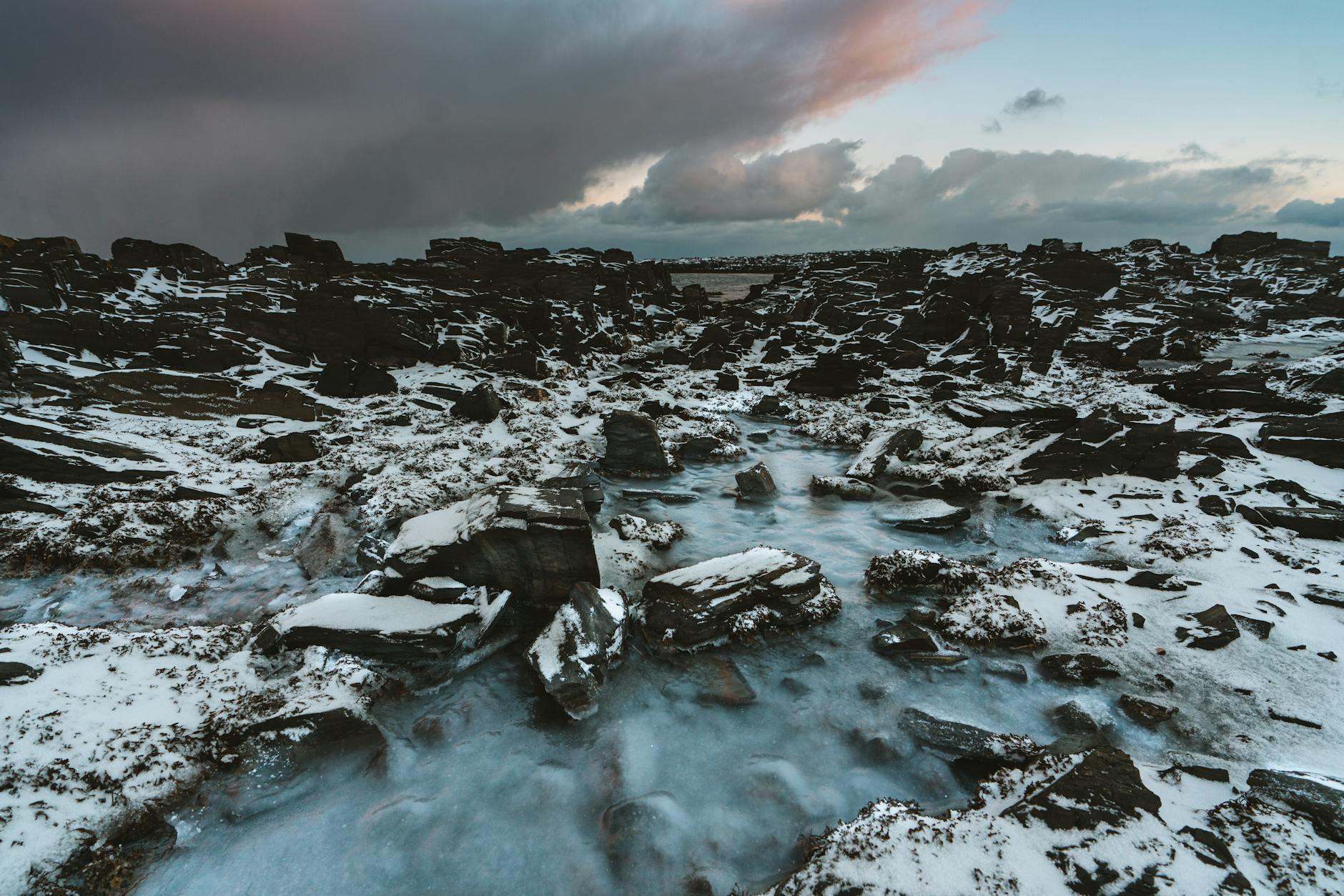 Serene arctic landscape featuring snow-laden rocks and a dramatic sky at dusk.