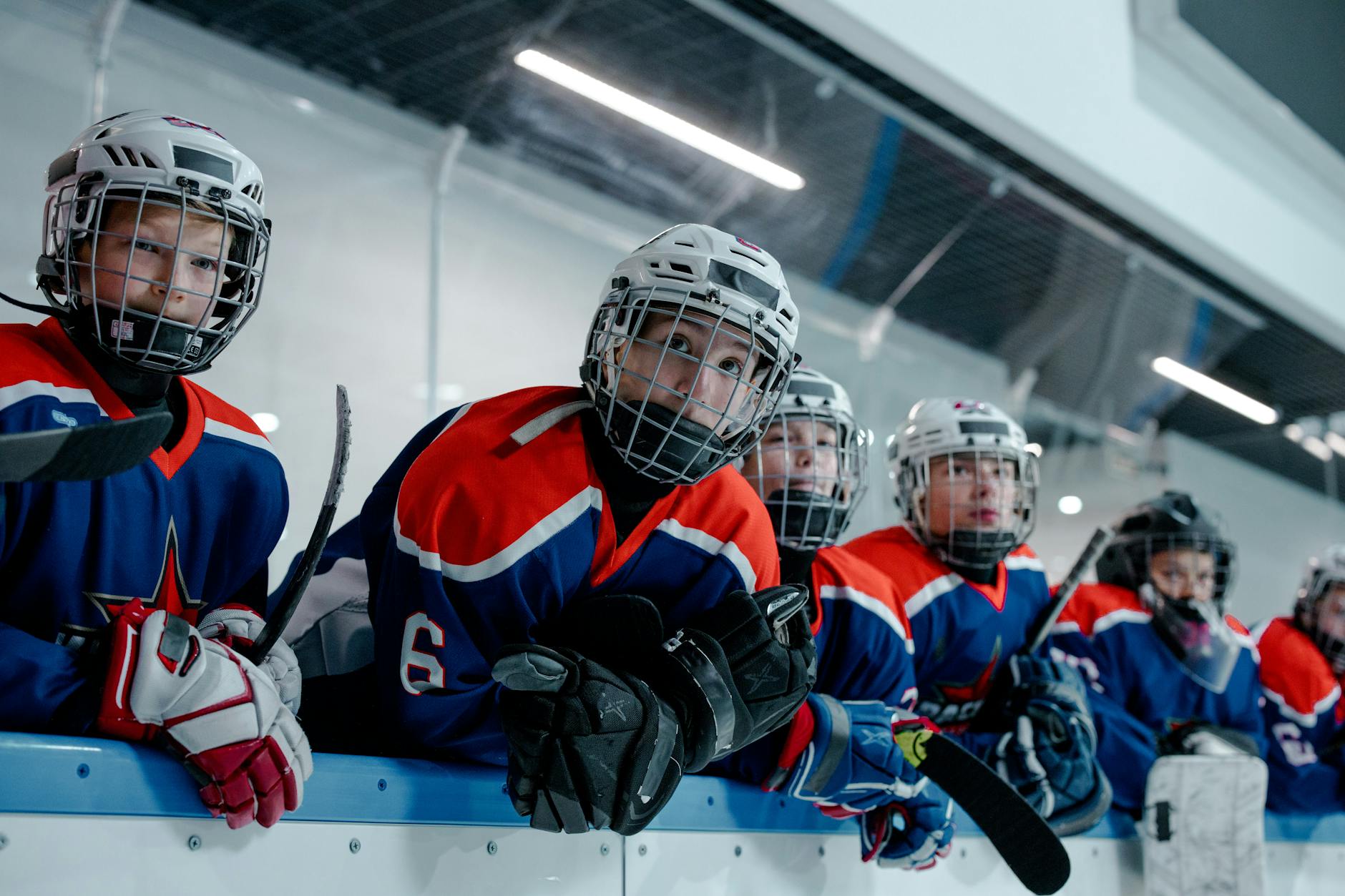 Energetic youth ice hockey team in blue and red uniforms eagerly waits by the rink.