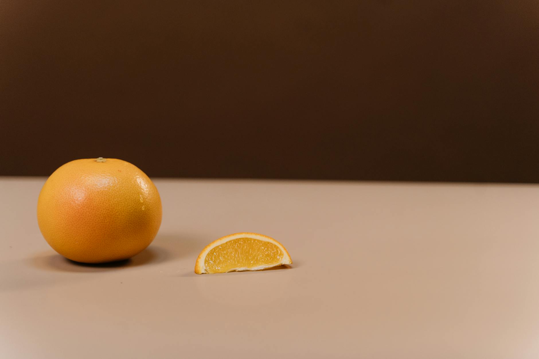 A simple still life of an orange and a slice on a neutral background, perfect for food and design projects.