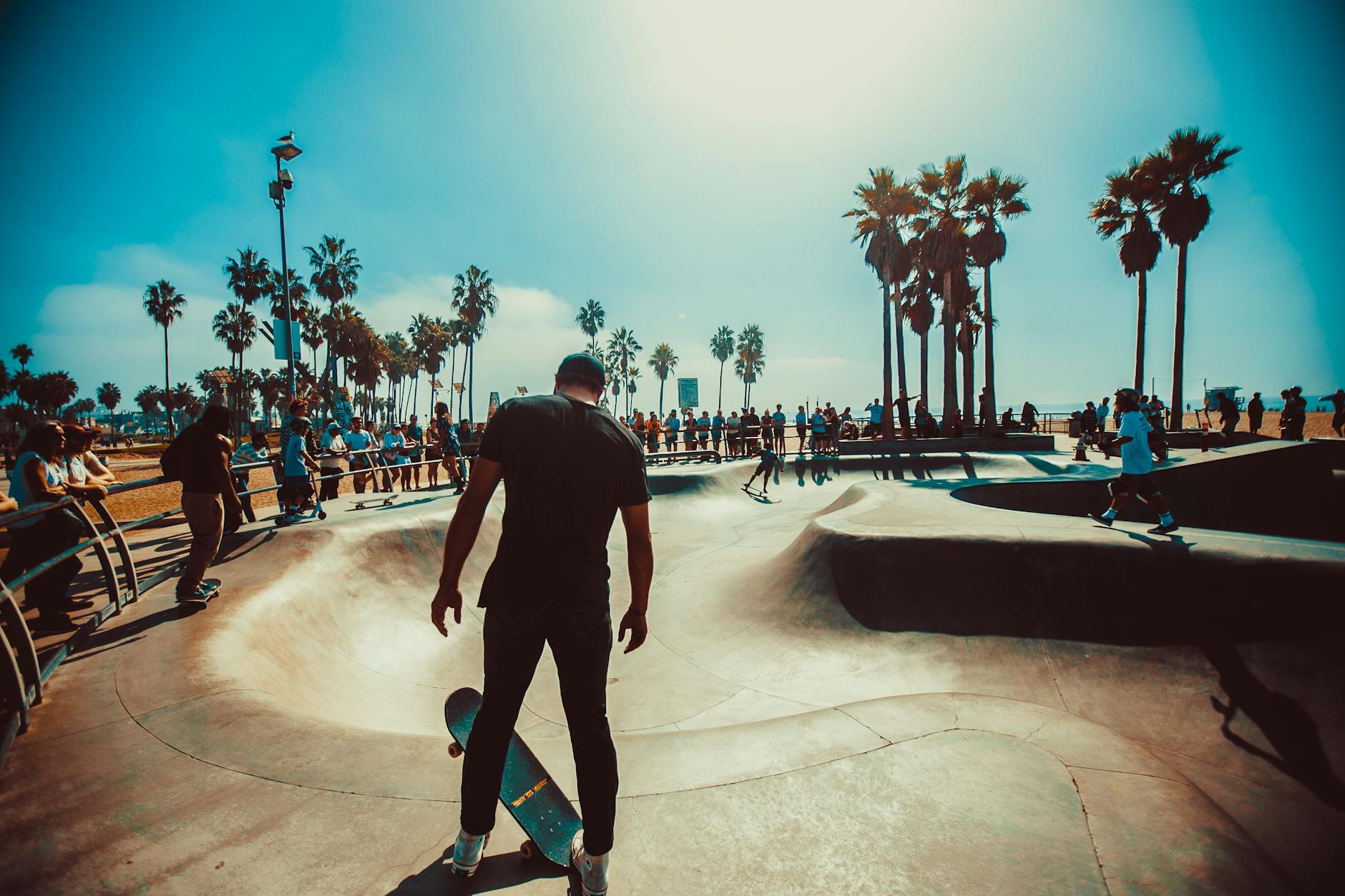 A skateboarder shows off skills in a bustling outdoor park on a sunny day.