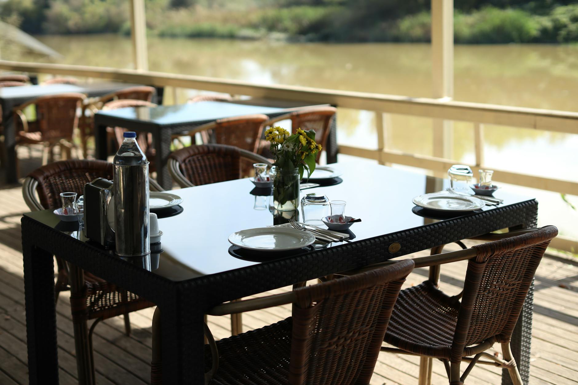 Elegant outdoor cafe table by the river, set for dining with a serene backdrop.