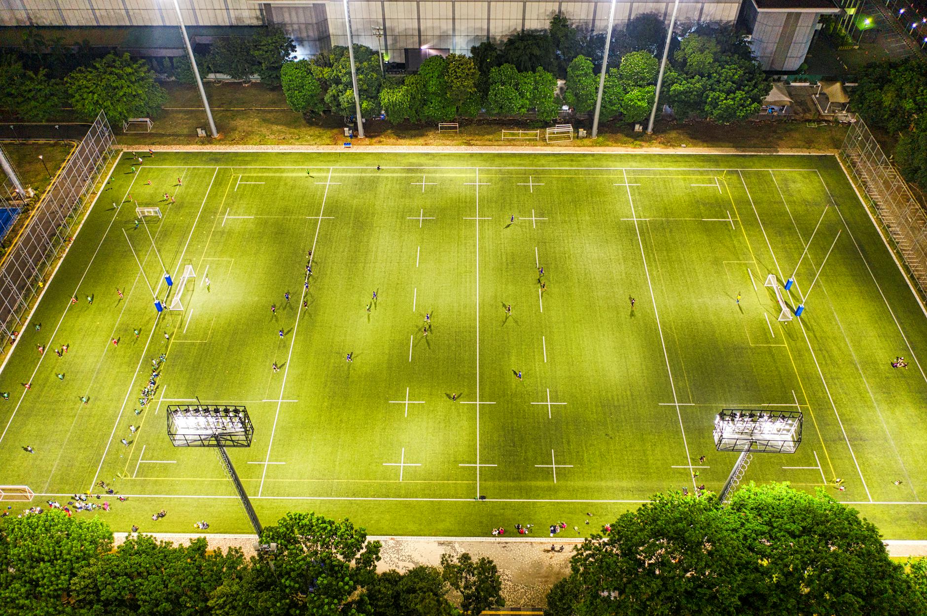Aerial view of a lit sports field at night in Jakarta, showcasing an ongoing match under bright stadium lights.