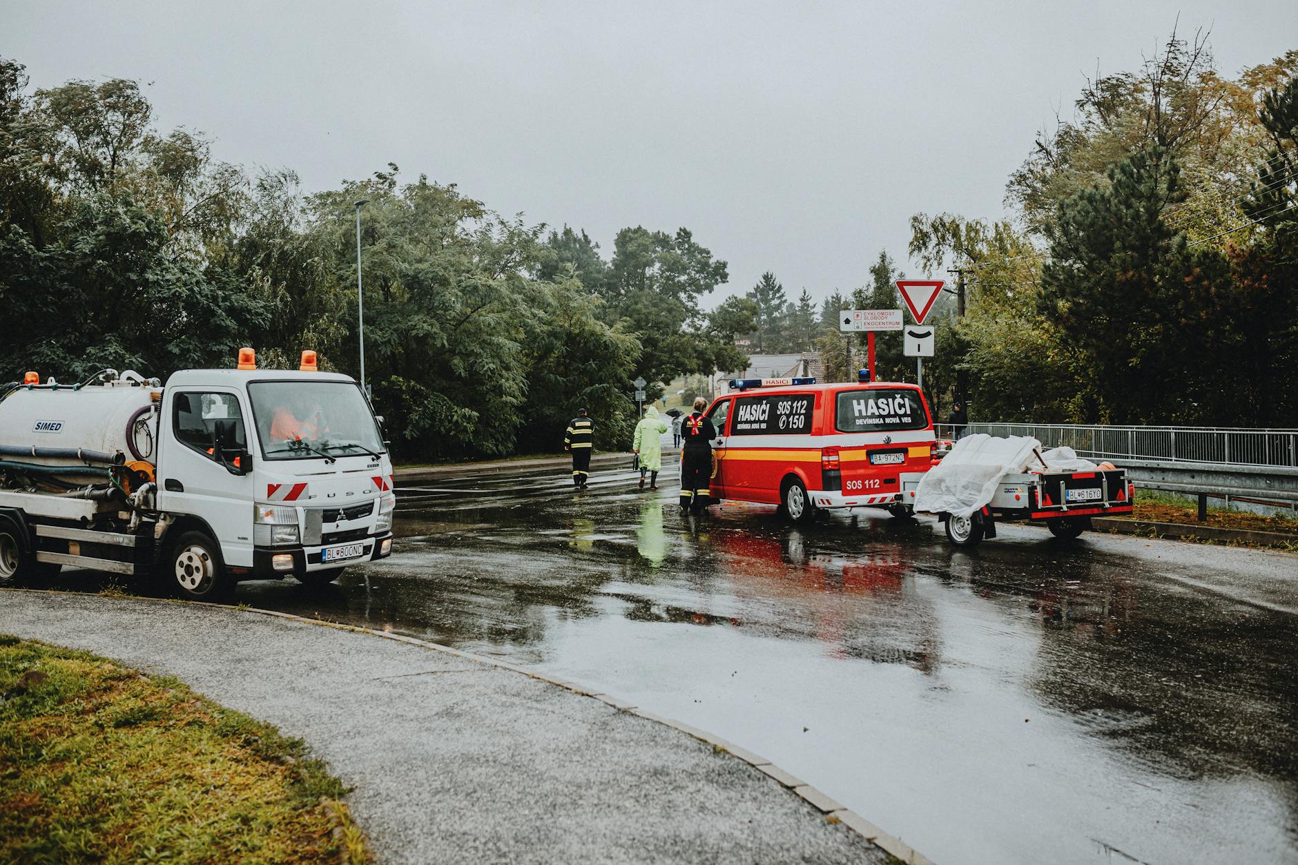Emergency services attending a scene on a rainy road with rescue vehicles and personnel.