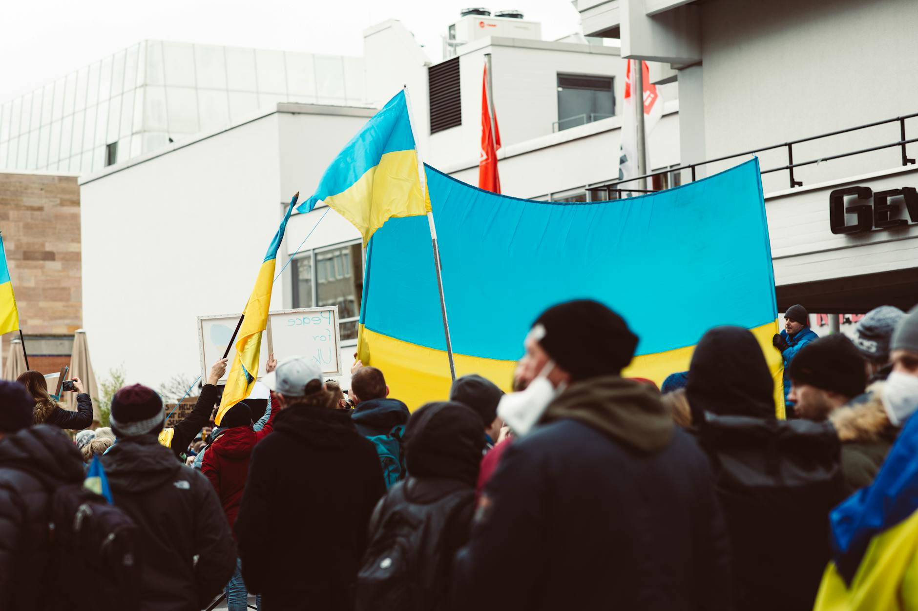 A large group of people rally outdoors holding Ukrainian flags during a peace protest.
