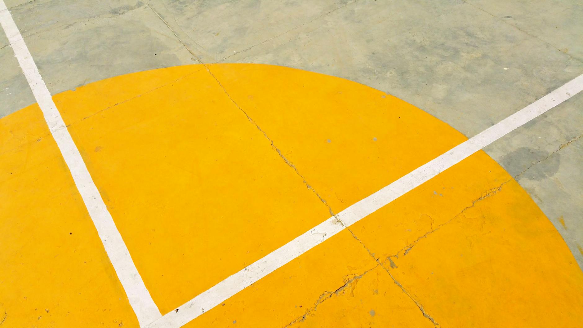 Close-up of a basketball court with yellow semicircle and white lines on concrete surface.