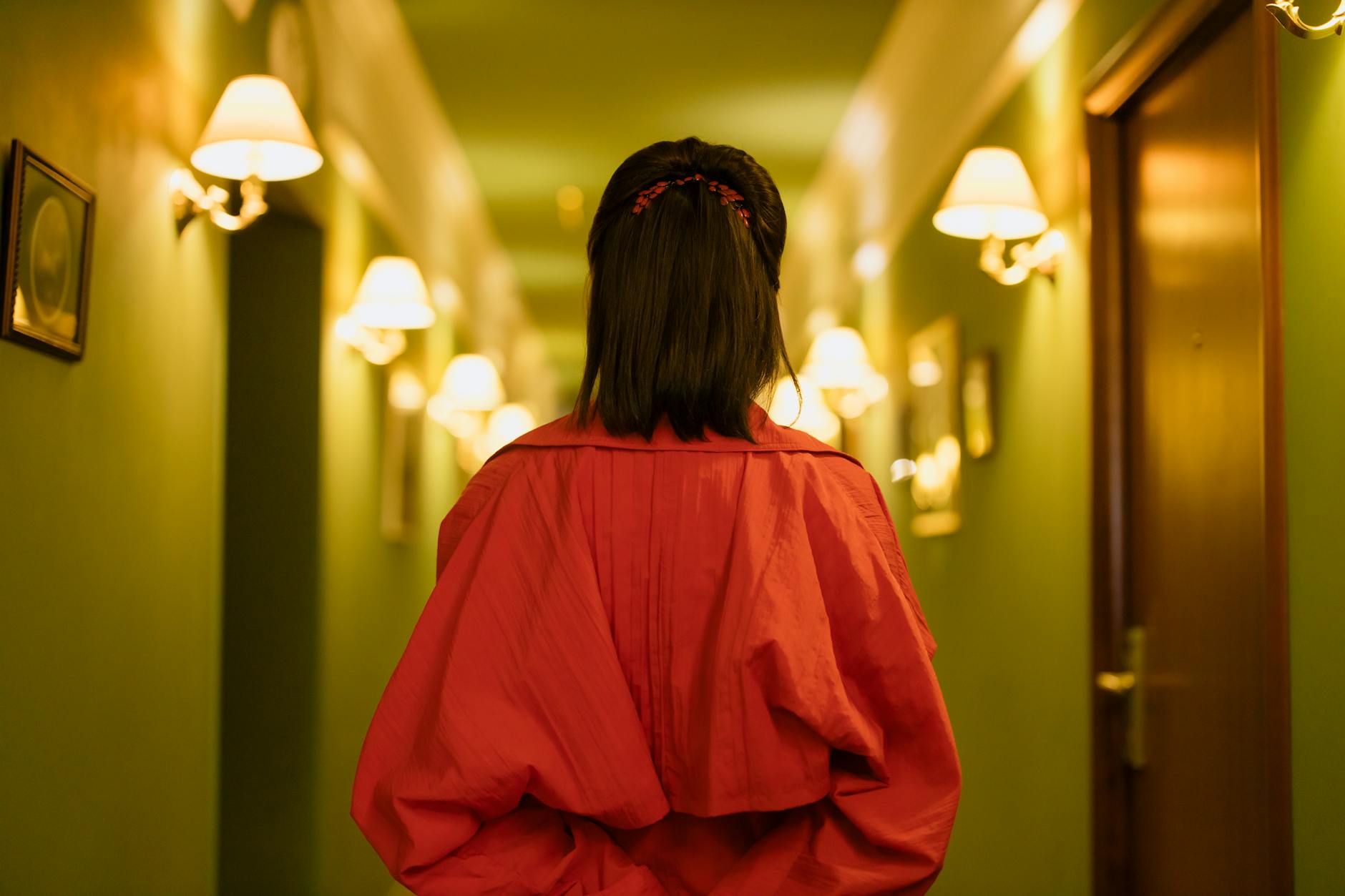 Stylish woman in a red dress walks through a well-lit hotel corridor, exuding elegance and poise.