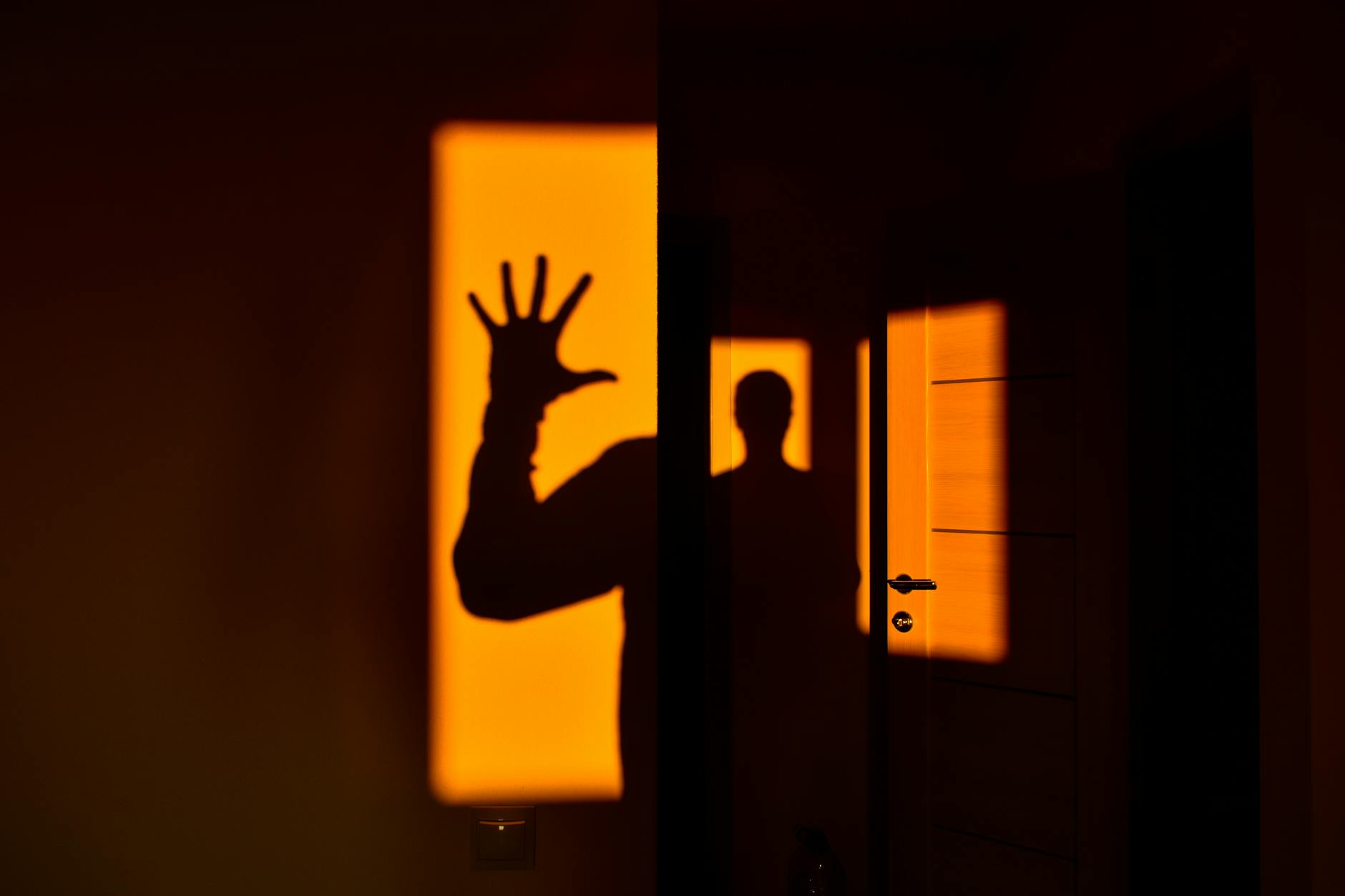 Silhouette of a person and hand forming a shadow on a vivid orange wall, evoking mystery.