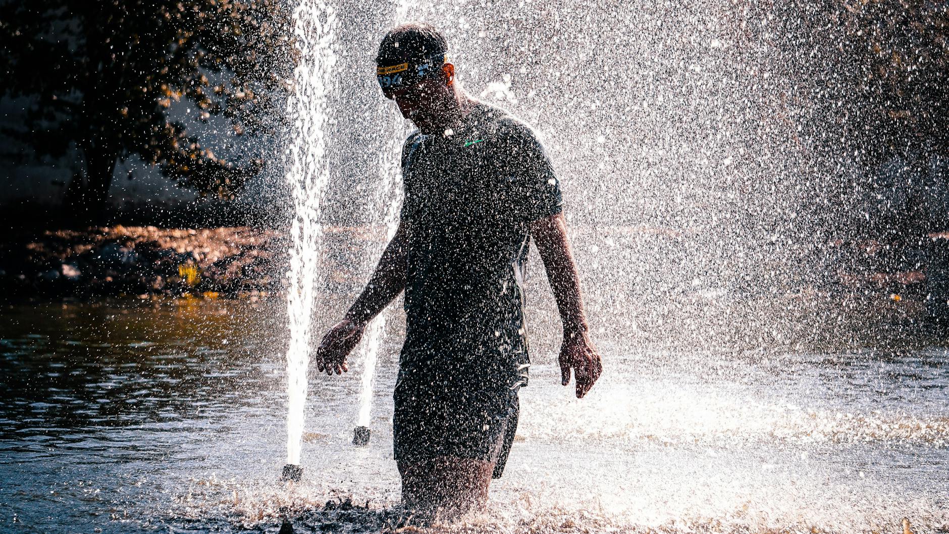 A man joyfully walks through a fountain, enjoying a refreshing splash on a sunny day.