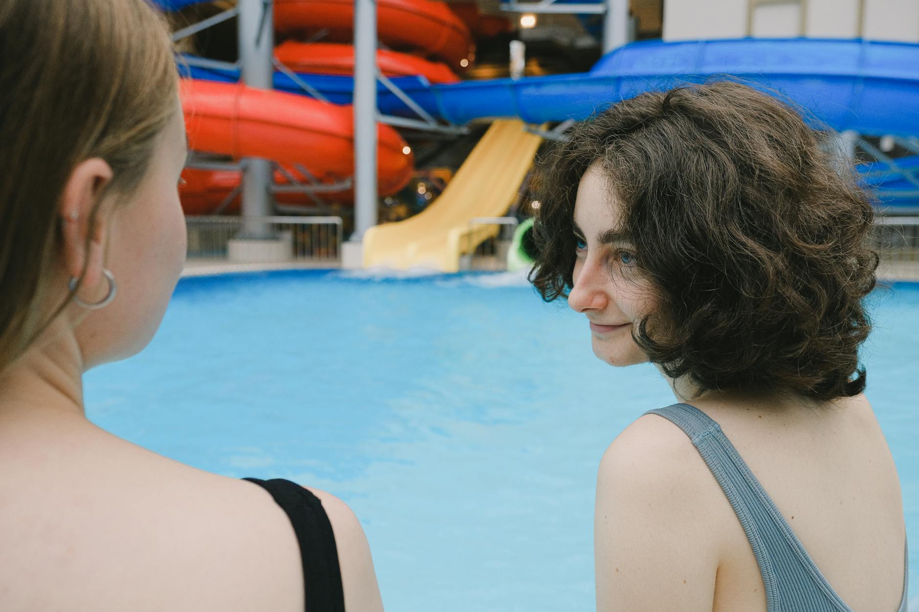 Two women enjoying leisure time next to a swimming pool surrounded by colorful water slides.