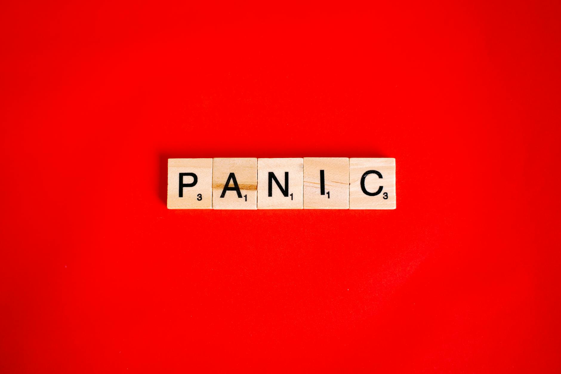 Scrabble tiles form the word 'panic' against a vibrant red backdrop, conveying urgency.